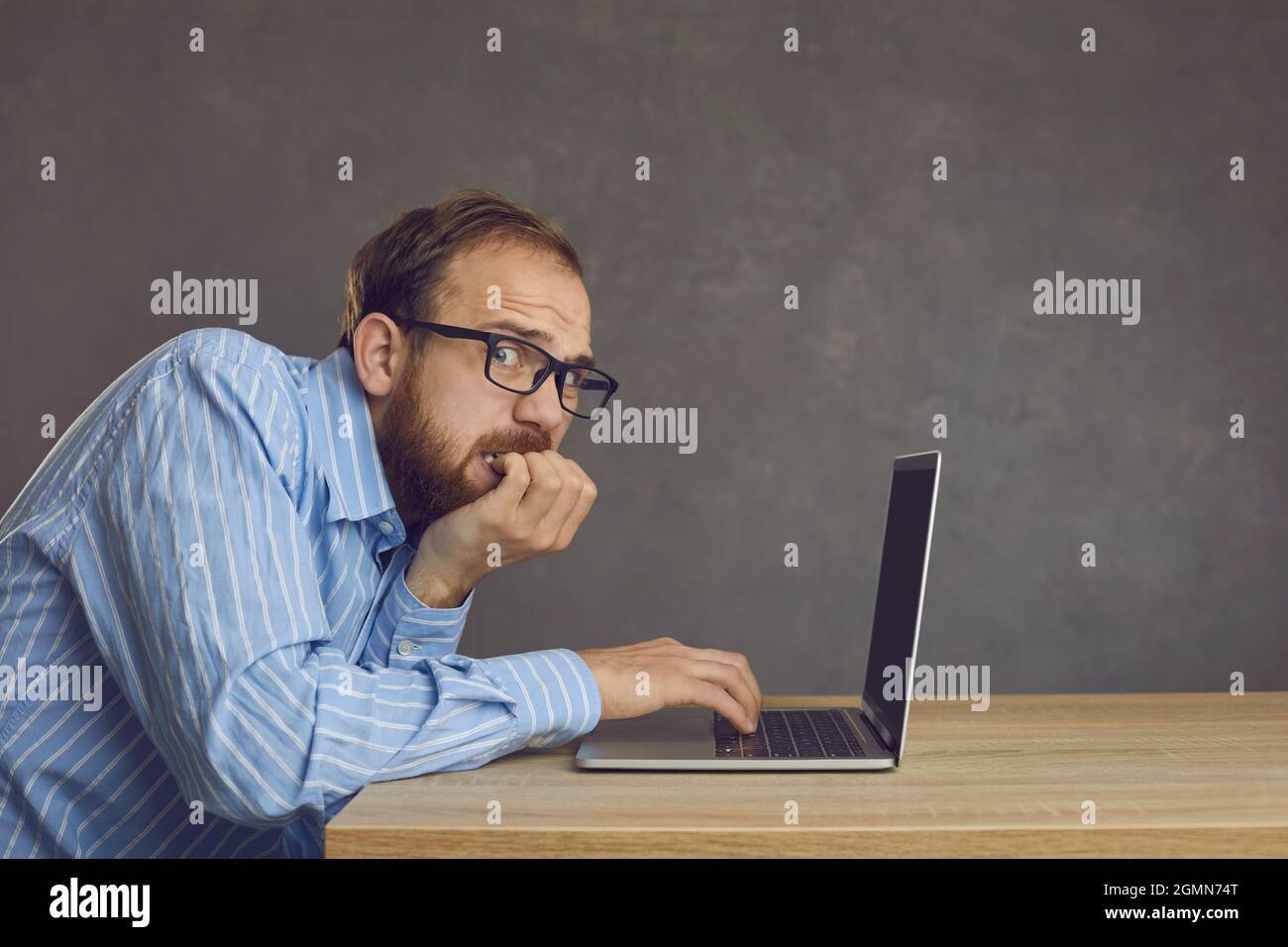 Erschrocken gestresster Mann, der einen Fehler gemacht hat, Nägel beißend, sitzend am Schreibtisch mit Laptop Stockfoto