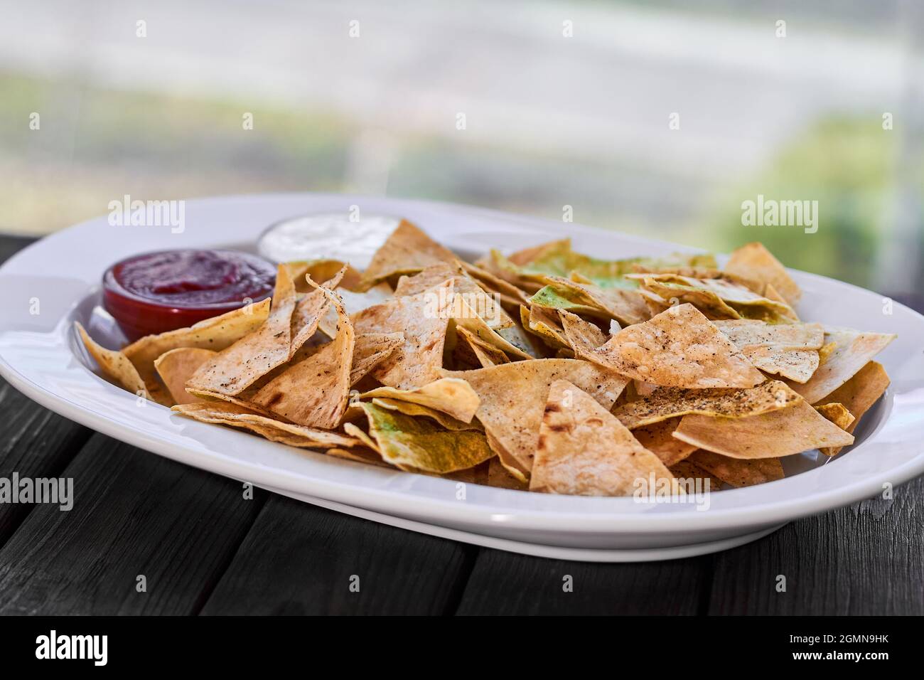 Dreieckige Nachos-Chips mit Tomatenketchup und Käsesauce auf weißem Teller und Holzboden Stockfoto