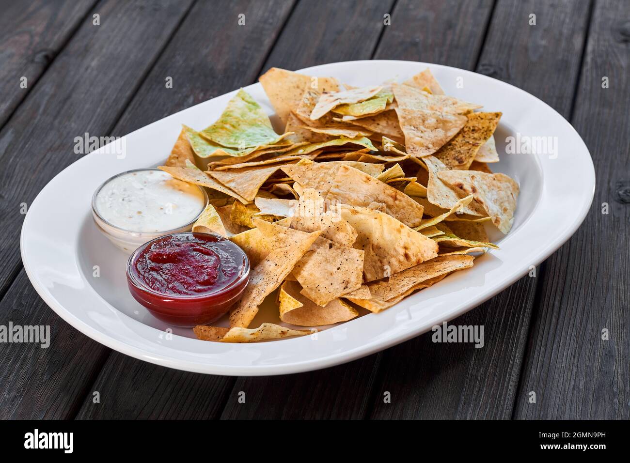 Dreieckige Nachos-Chips mit Tomatenketchup und Käsesauce auf weißem Teller und Holzboden Stockfoto