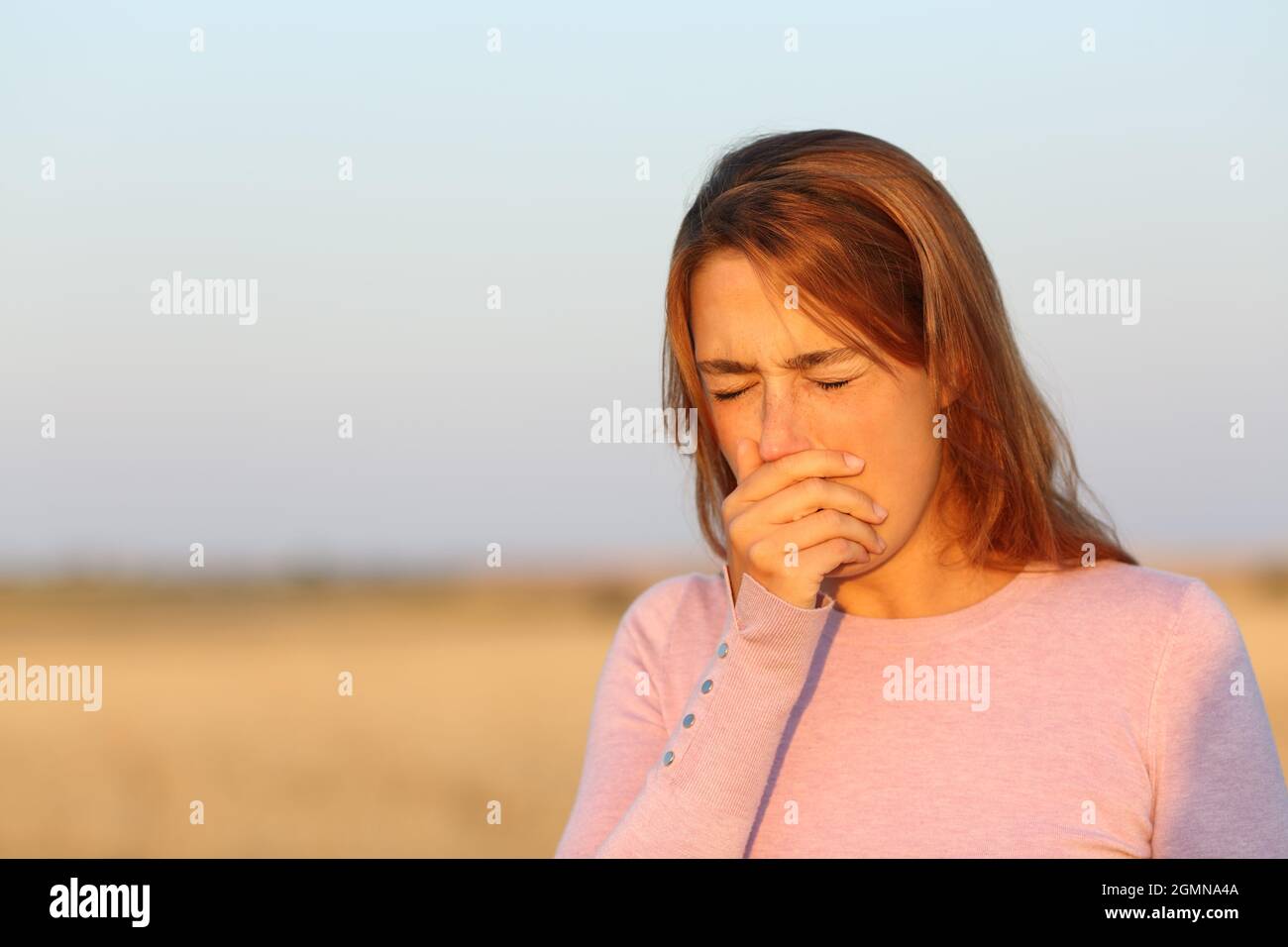 Kranke Frau, die bei Sonnenuntergang auf einem geernteten Feld hustet Stockfoto