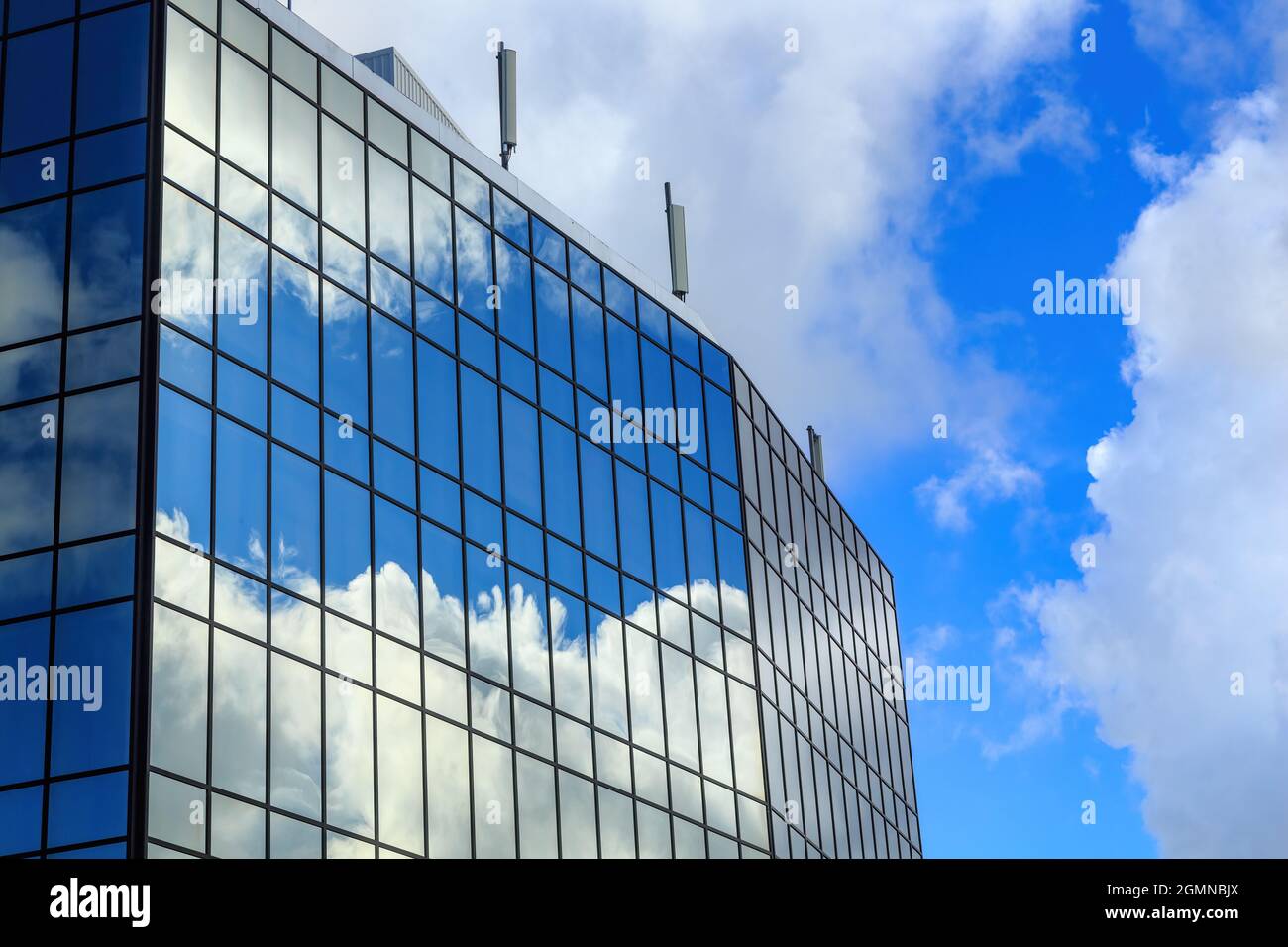 Blauer Himmel und flauschige Wolken spiegeln sich in den Fenstern eines Spiegelglasgebäudes Stockfoto