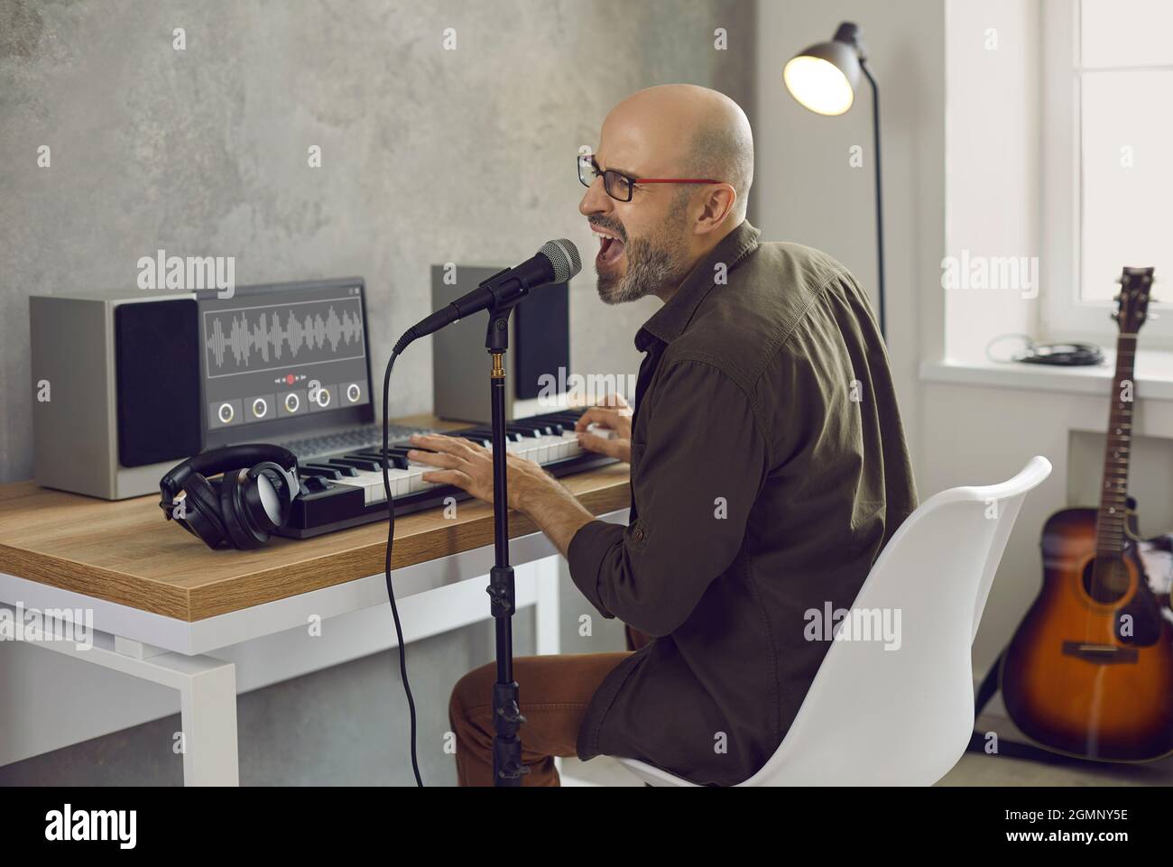 Musiker singt und spielt Musik auf MIDI-Keyboard in seinem Aufnahmestudio zu Hause Stockfoto