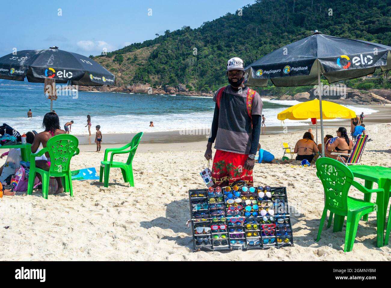 Ein brasilianischer Mann, der am Strand von Piratininga in Rio de Janeiro, Brasilien, Sonnenbrillen verkauft. Mit einer wunderschönen Landschaft ist dieser berühmte Ort ein großer touris Stockfoto
