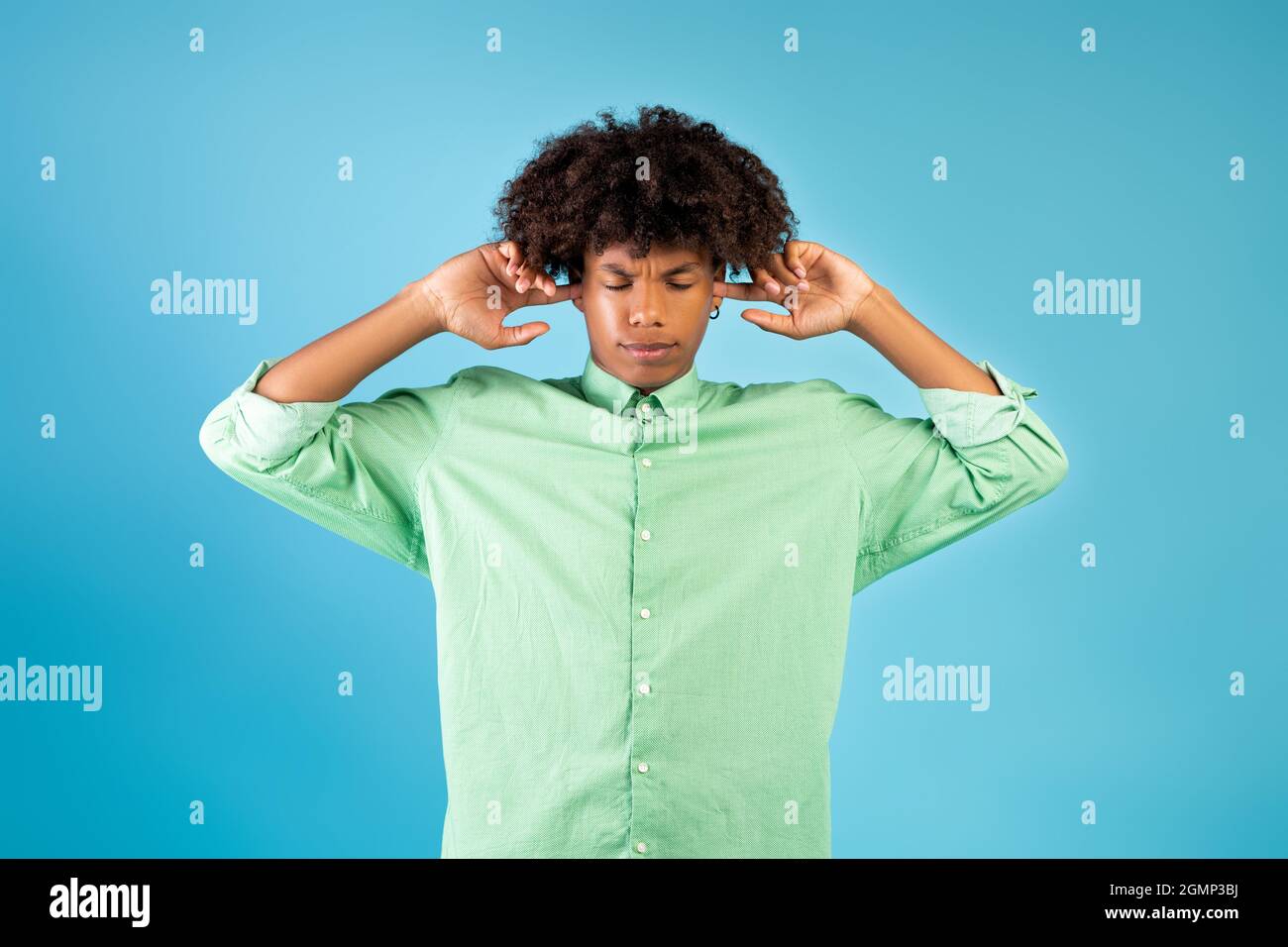 Verstörter afroamerikanischer Kerl, der seine Ohren mit den Fingern schließt und sich vor lauten Geräuschen über blauem Studiohintergrund schützt Stockfoto
