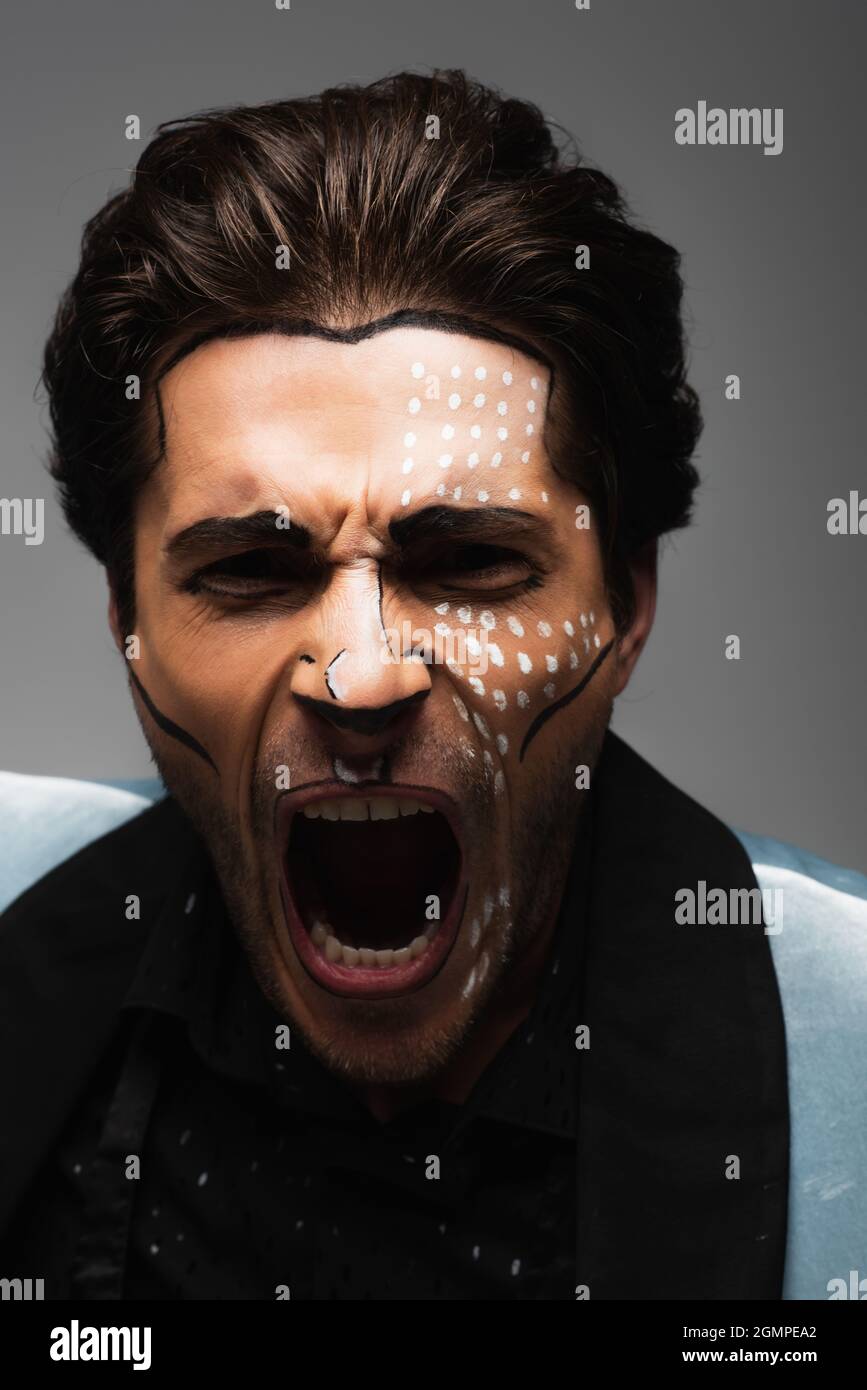 Wütender Mann in halloween Make-up schreiend auf Kamera isoliert auf grau Stockfoto