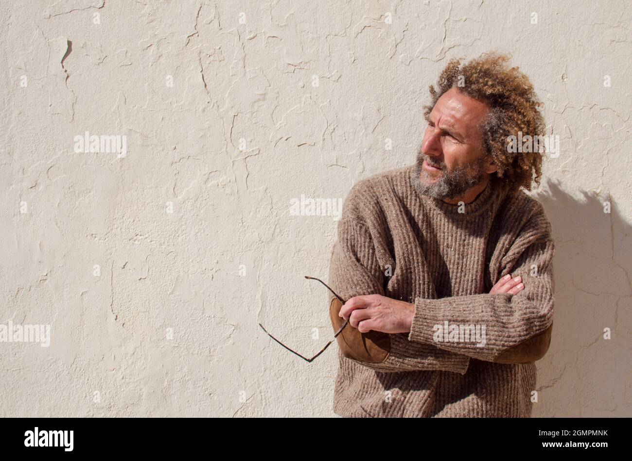 Ein Mann mittleren Alters blickt introspektiv zur Seite und hält eine Brille in den Händen Stockfoto