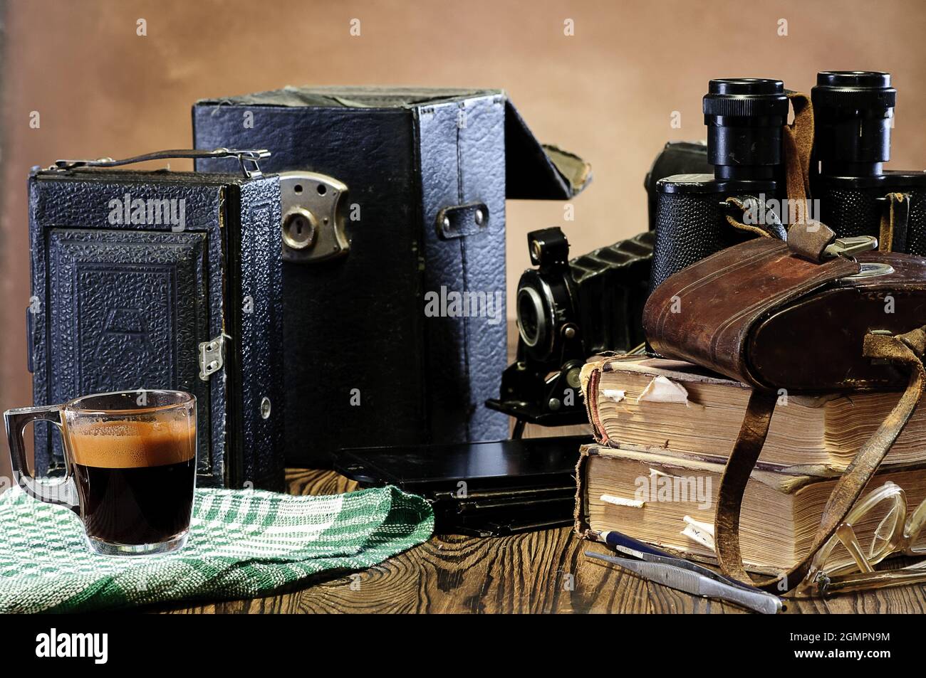 Stapel alter Bücher, Ferngläser, Vintage-Kamera, ausgefranste Ledertaschen auf einem Holztisch Stockfoto