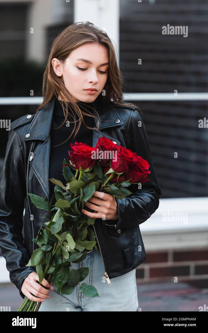 Hübsche junge Frau in Lederjacke mit Blick auf rote Rosen auf der  städtischen Straße in europa Stockfotografie - Alamy