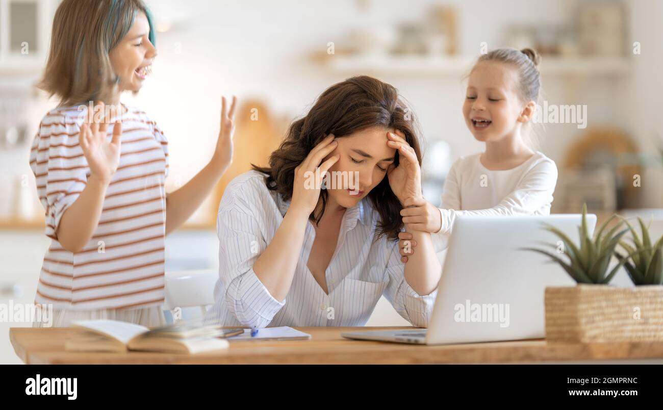 Frau, die an einem Laptop arbeitet. Laute Kinder und Fernarbeit von zu Hause aus. Stockfoto