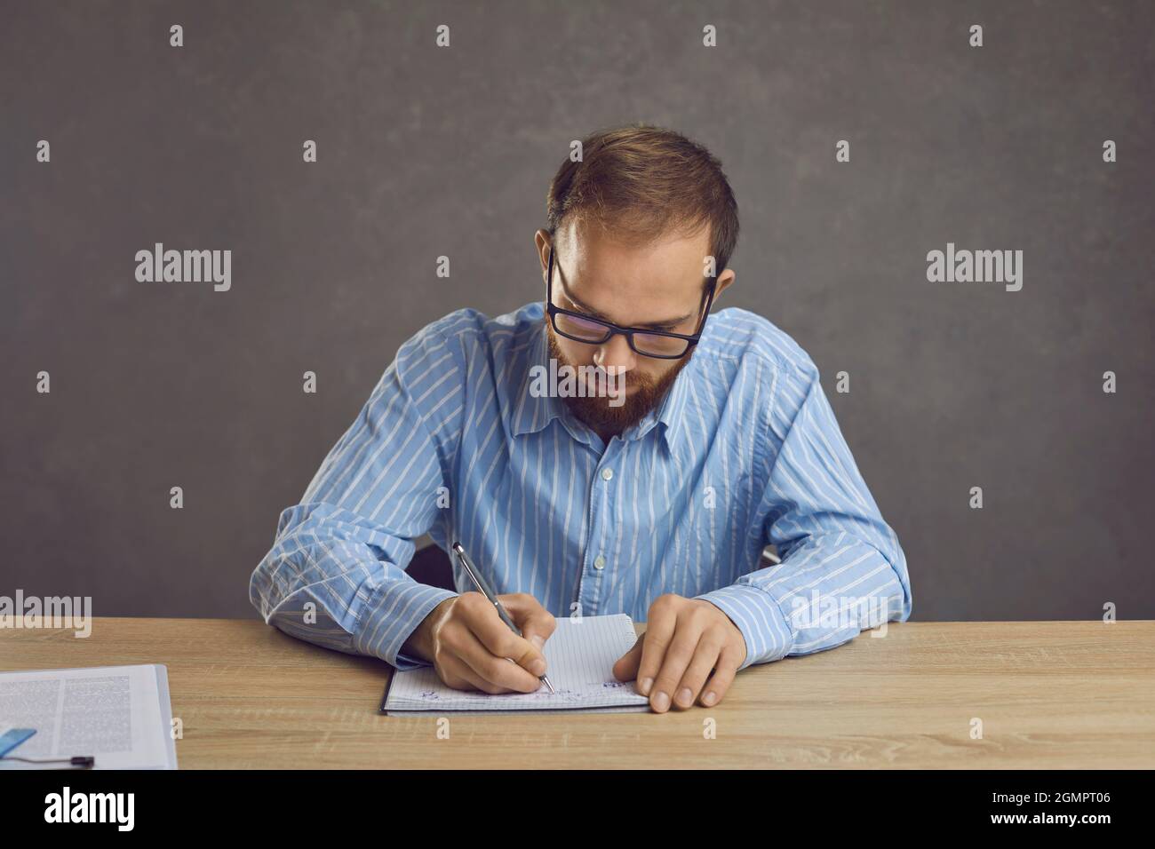Seriös junger Mann in Brille sitzt an einem Tisch und Notizen in seinem Notizbuch Stockfoto