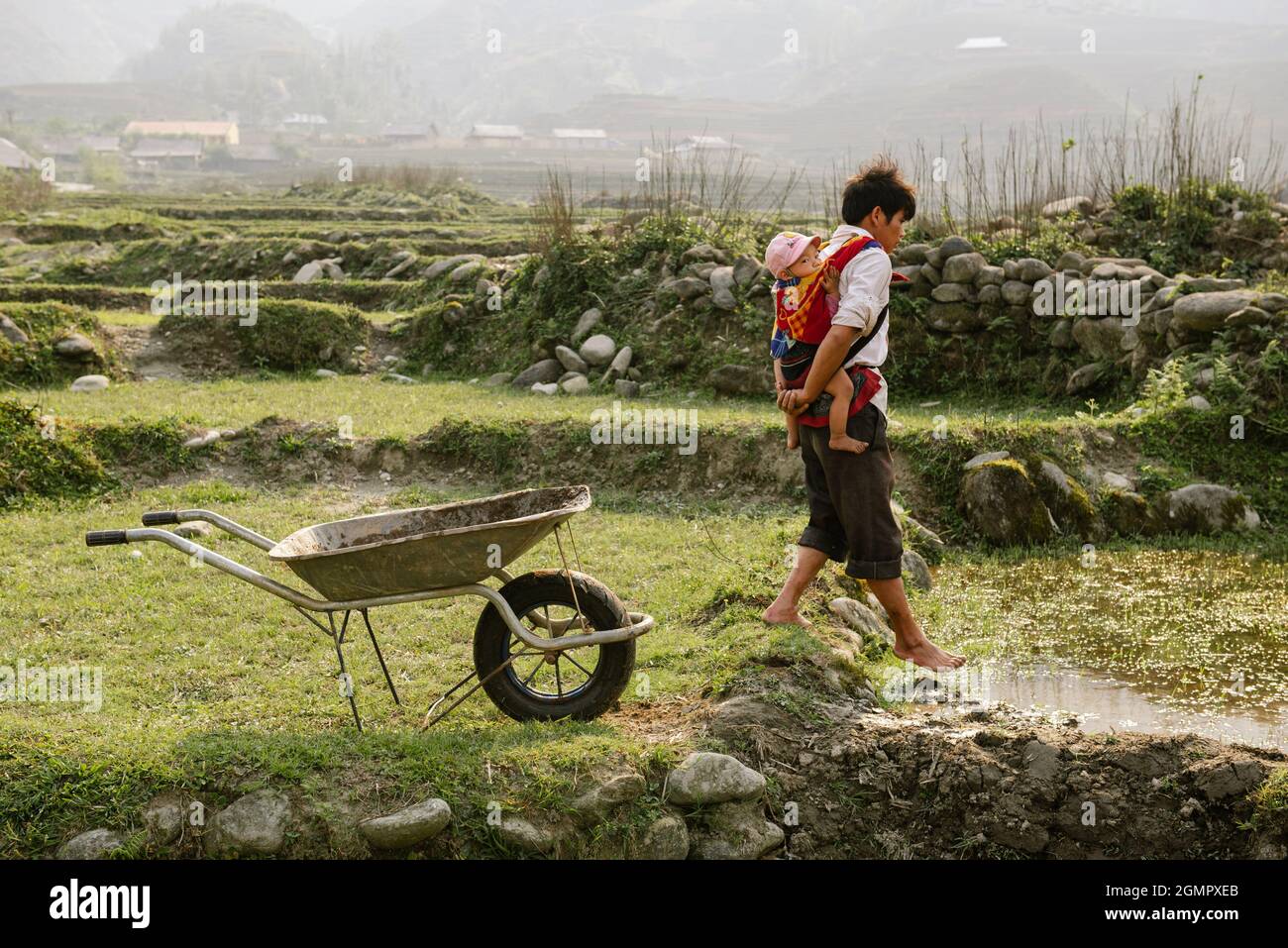 Sapa, Vietnam - 14. April 2016: Vietnamesischer Vater mit Kind, das auf dem Feld arbeitet, während seine Frau arbeitet. Vaterschaft in Asien, ländliche arme Gegend Stockfoto