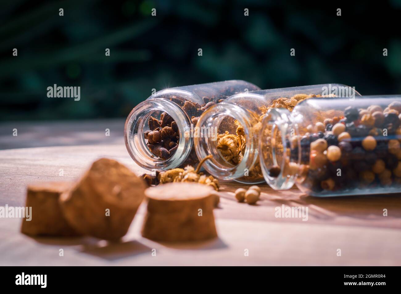 Ein Bild von drei Glasflaschen mit Pfefferkörnern, Kamille und Nelken, die auf einer Holzoberfläche auslaufen Stockfoto