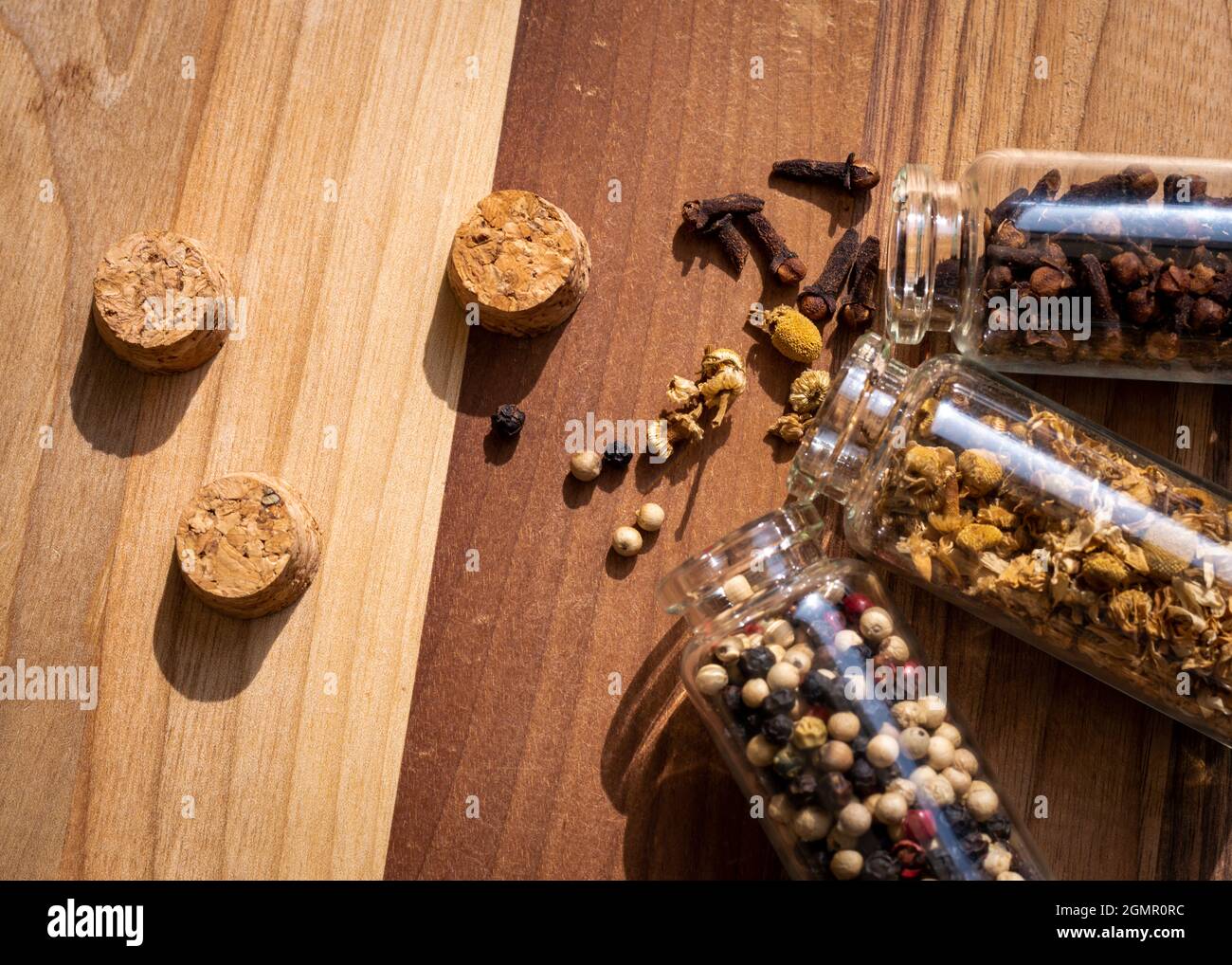 Ein Bild von drei Glasflaschen mit Pfefferkörnern, Kamille und Nelken, die auf einer Holzoberfläche auslaufen Stockfoto