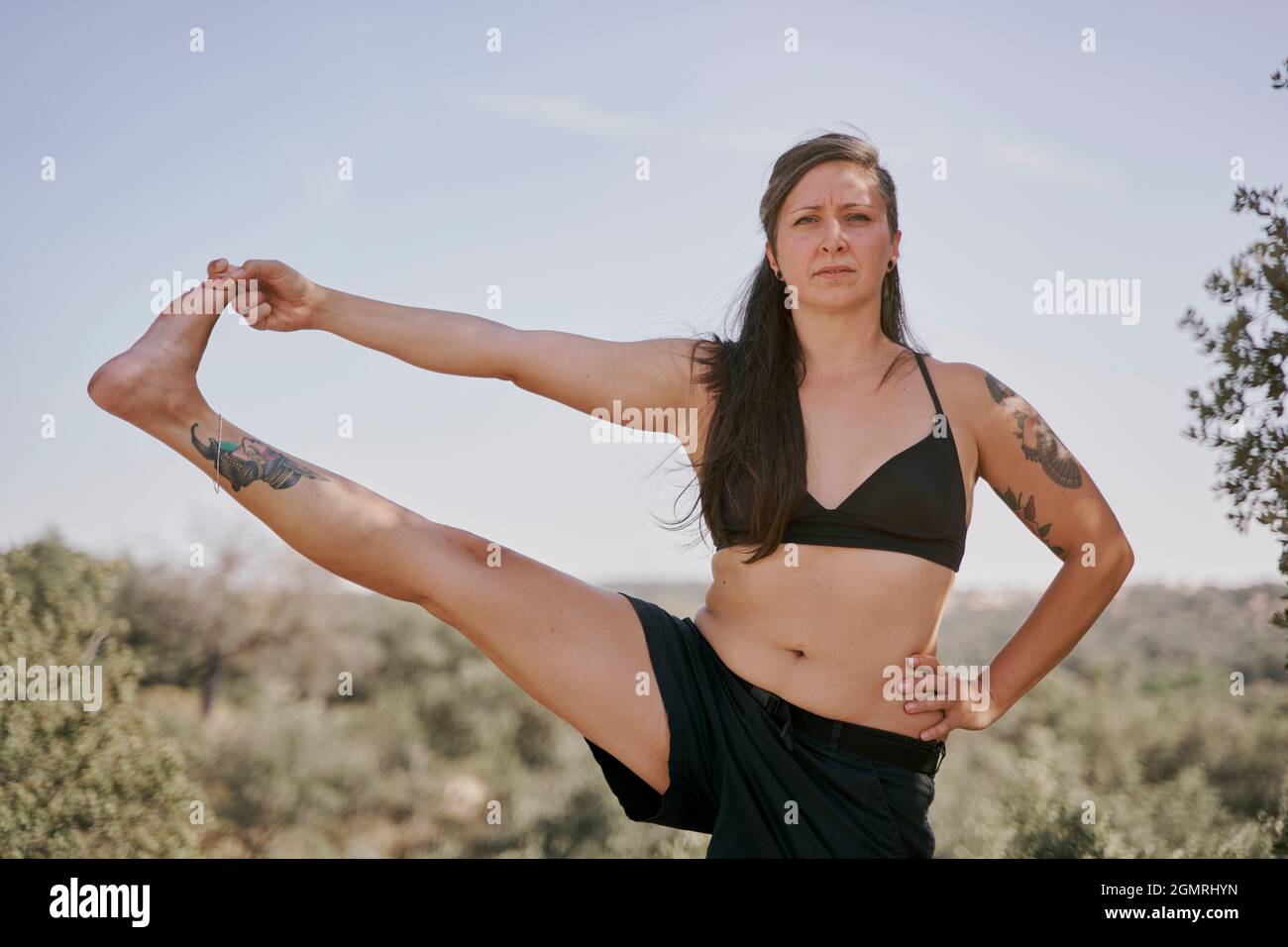 Gesunde Frau, die Yoga in der Natur praktiziert. Sportliche Frau in Yoga-Haltung mit einem Bein angehoben. Utthita Hasta Padangusthasana Stockfoto