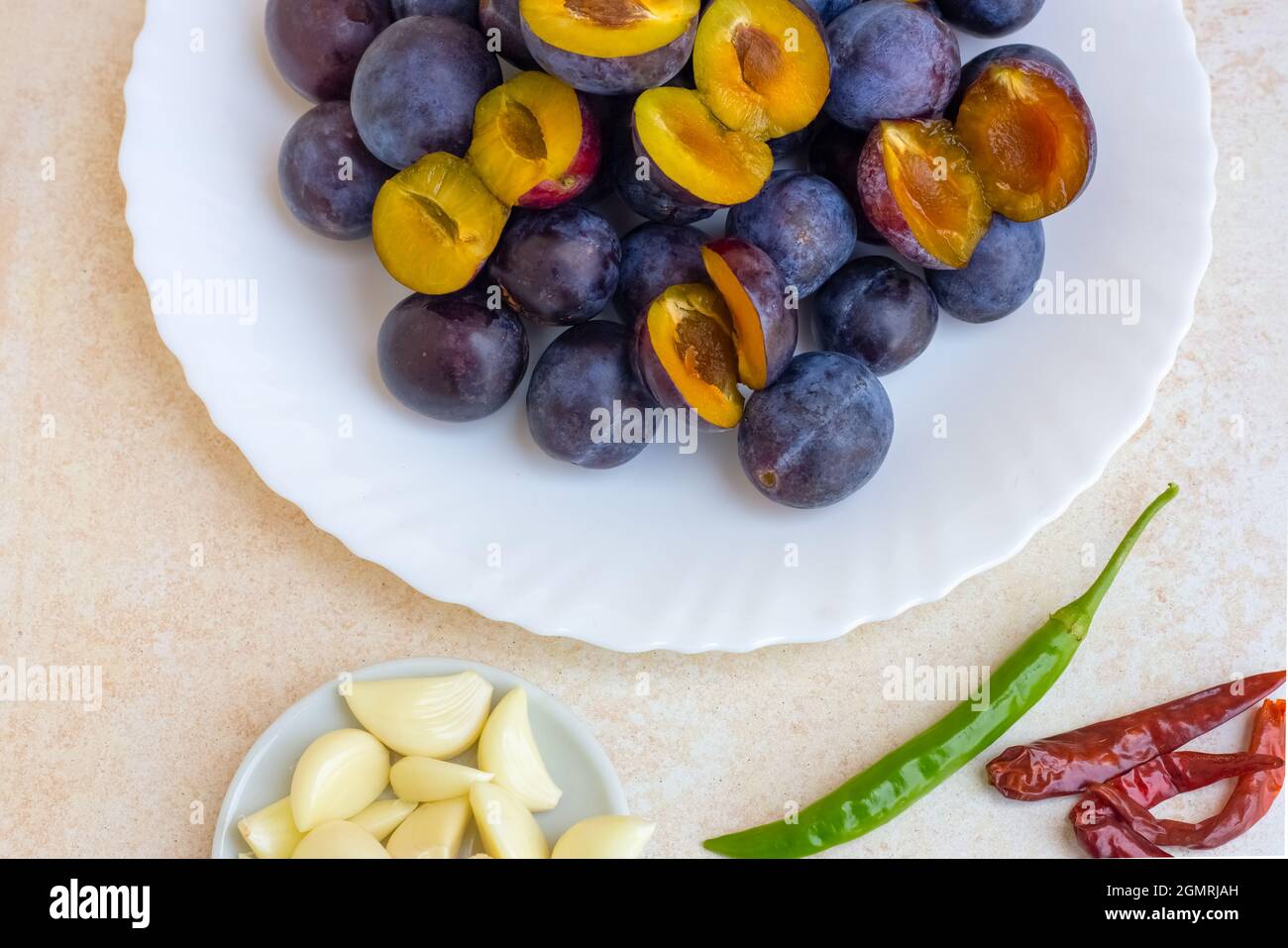 Eine Reihe von Produkten für die Herstellung von würzigen Obst georgischen Sauce tkemale. Pflaumen auf einem Teller, Knoblauch und Paprika in der Nähe. Stockfoto