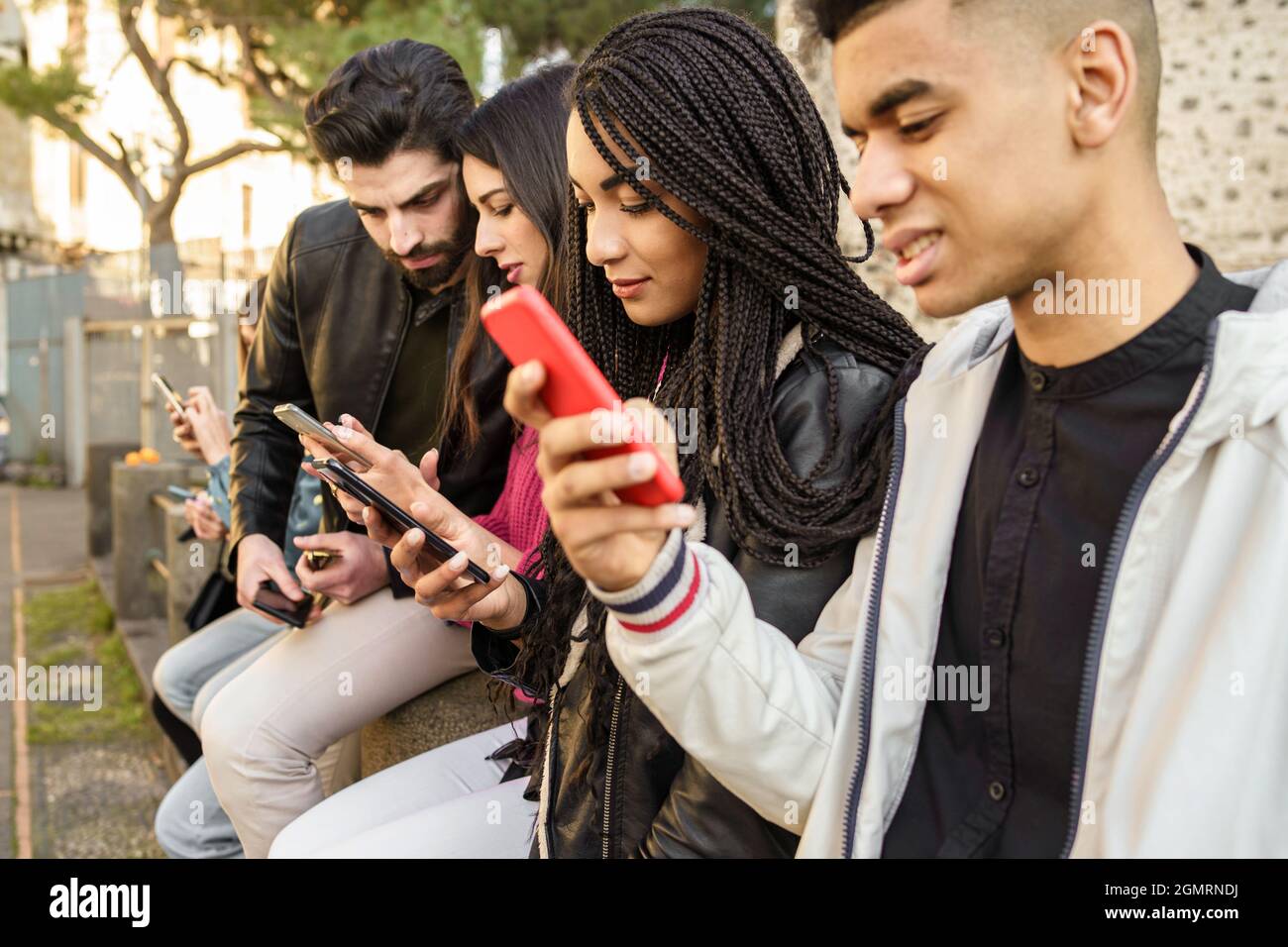 Generation z junge Menschen süchtig nach Smartphone und neuer Technologie. Gruppe von jungen Menschen mit gemischter Gruppe, die im Freien mit einem Mobiltelefon in den Händen sitzen. Te Stockfoto