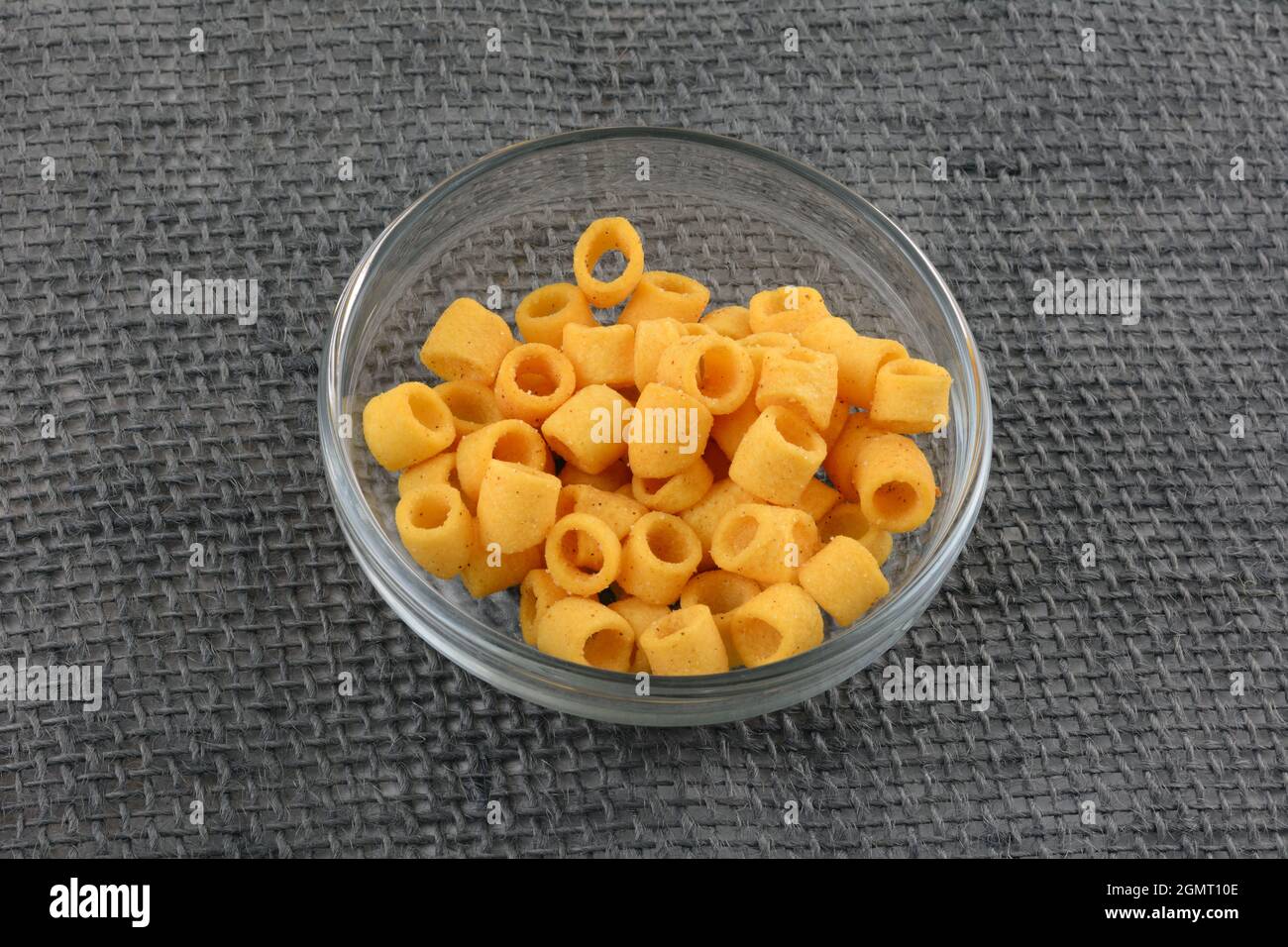Knusprige Grillkartoffelringe in Glas-Snack-Schale auf grauem Sackleinen-Tuch Stockfoto