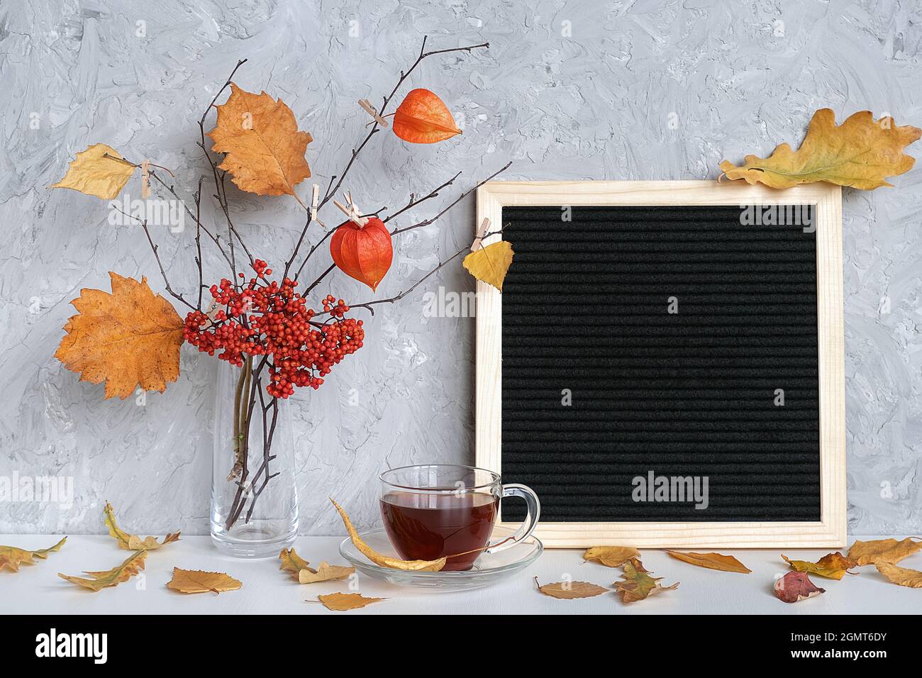 Unbeschriftete schwarze Brillengestell und Herbststrauß von Ästen mit gelben Blättern auf Wäscheklammern in Vase, Tasse Tee auf Tisch Mockup Template für Ihre Stockfoto