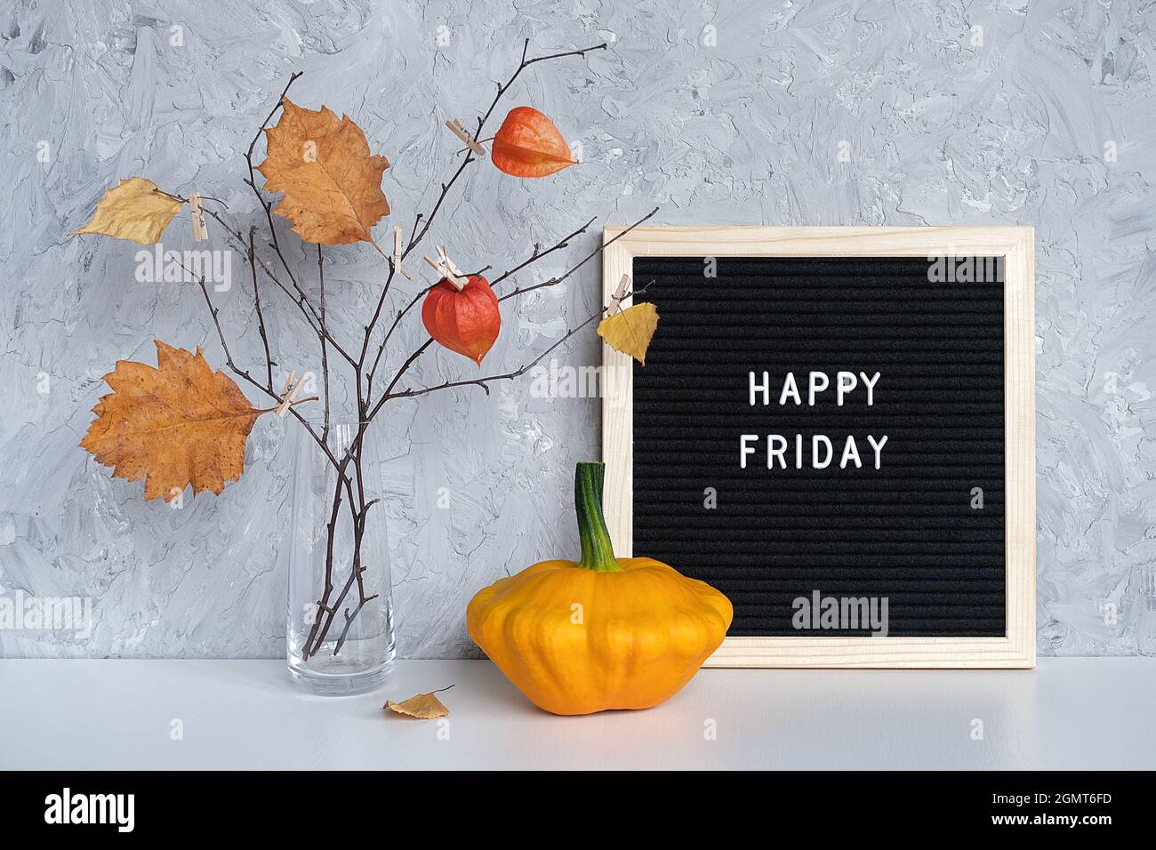 Happy Friday Text auf schwarzem Briefbrett und Strauß von Zweigen mit gelben Blättern auf Wäscheklammern in Vase auf Tisch Vorlage für Postkarte, Gruß Auto Stockfoto