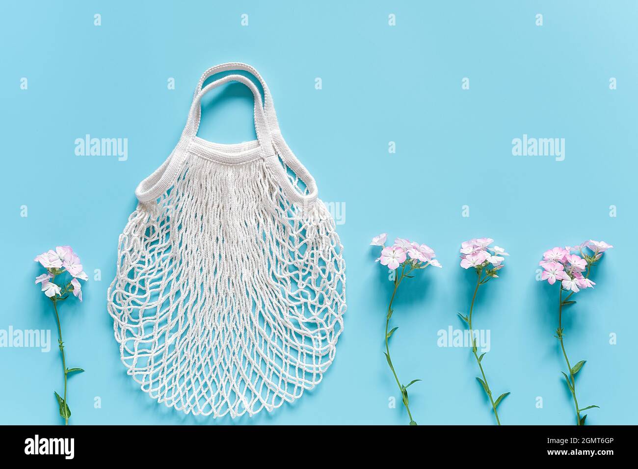 Zarte Blumen und weiße wiederverwendbare Einkaufstasche aus Öko-Mesh auf blauem Hintergrund. Konzept kein Kunststoff, keine Verschwendung und Pflege der Umwelt. Speicherplatz kopieren nach Stockfoto