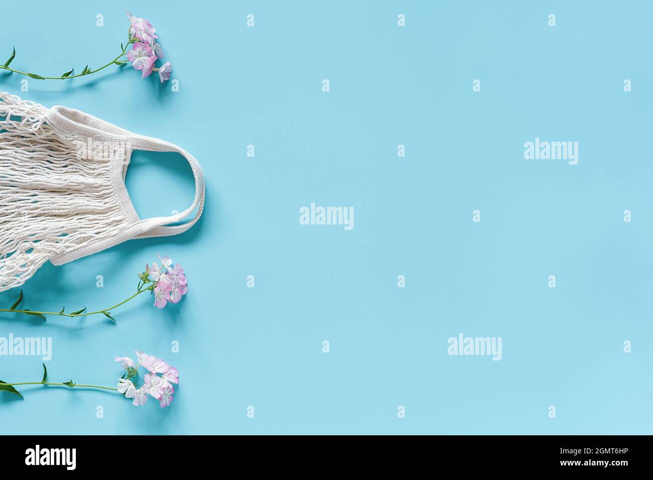 Zarte Blumen und weiße wiederverwendbare Einkaufstasche aus Öko-Mesh auf blauem Hintergrund. Konzept kein Kunststoff, keine Verschwendung und Pflege der Umwelt. Speicherplatz kopieren nach Stockfoto