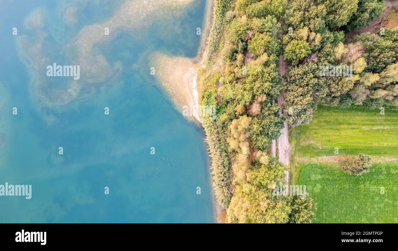 Luftaufnahme eines malerischen Ortes, an dem im Frühling das durchsichtige türkisfarbene Wasser eines Waldsees auf ein steineres Ufer mit Bäumen trifft. Aufgenommen mit einer Drohne. Hochwertige Fotos Stockfoto