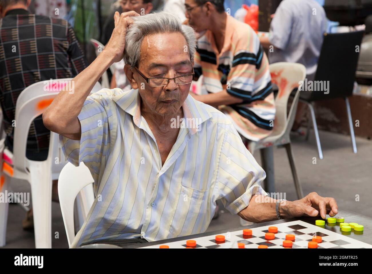 Chinatown, Singapur - 1. April 2011 auf diesem lauten, offenen Platz im Zentrum von Singapurs Chinatown konzentrierte sich der rauchende Mann auf sein Schachspiel Stockfoto