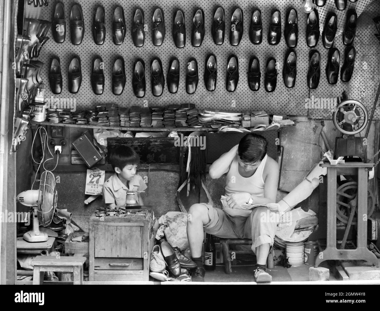 Hongkong, China - 13. Oktober 1983; ein Junge und sein Vater in einem Schusterstand. Dieses historische Schwarz-Weiß-Bild ist über 34 Jahre alt und illustriert Stockfoto