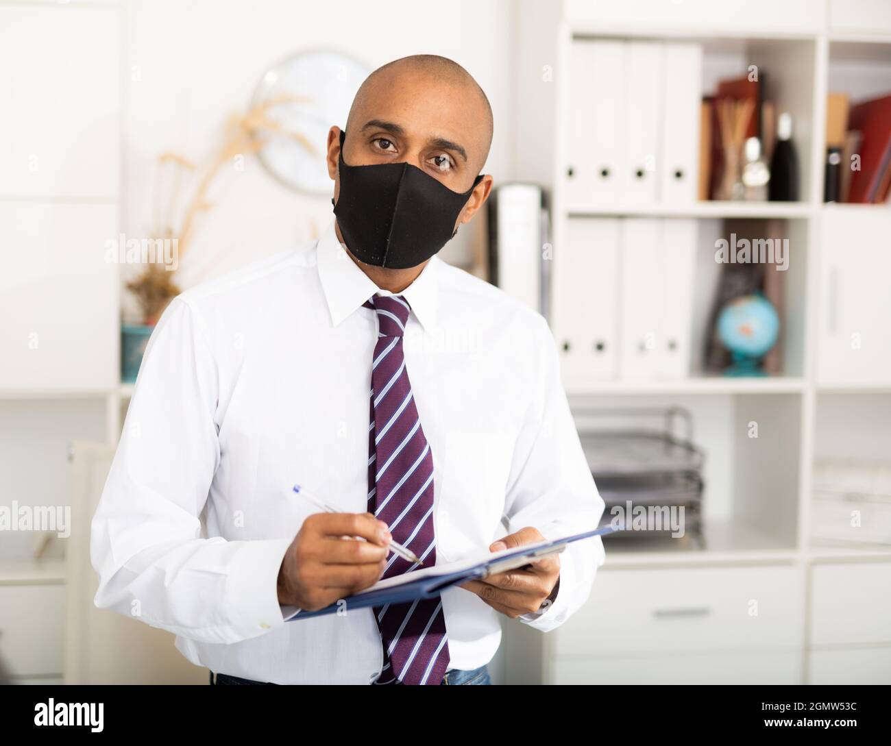 Geschäftsmann in Schutzmaske macht Notizen im Dokument Stockfoto