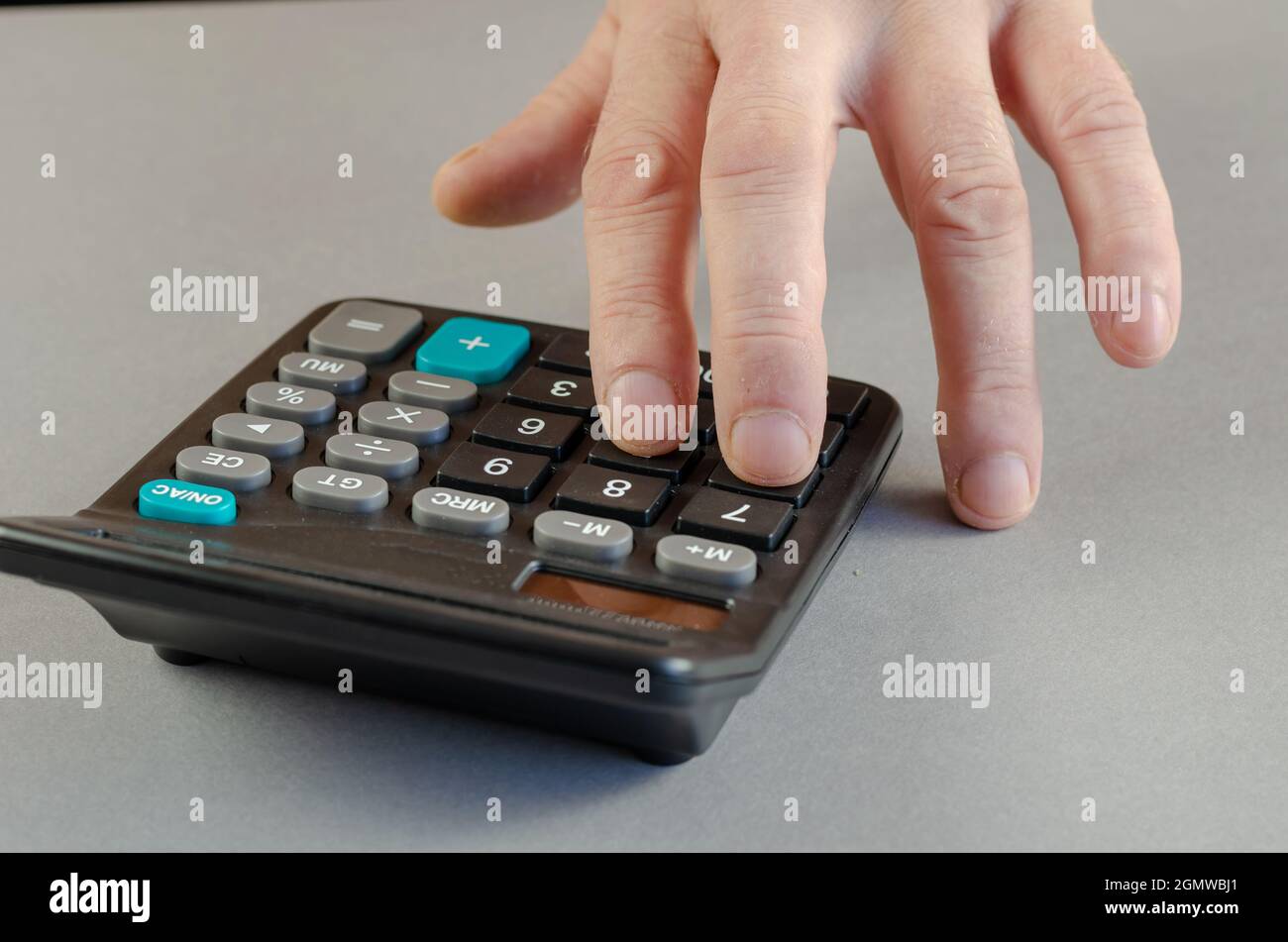 Die Hand eines Mannes zählt auf einen Rechner. Ein reifer Mann führt die Mathe durch Stockfoto