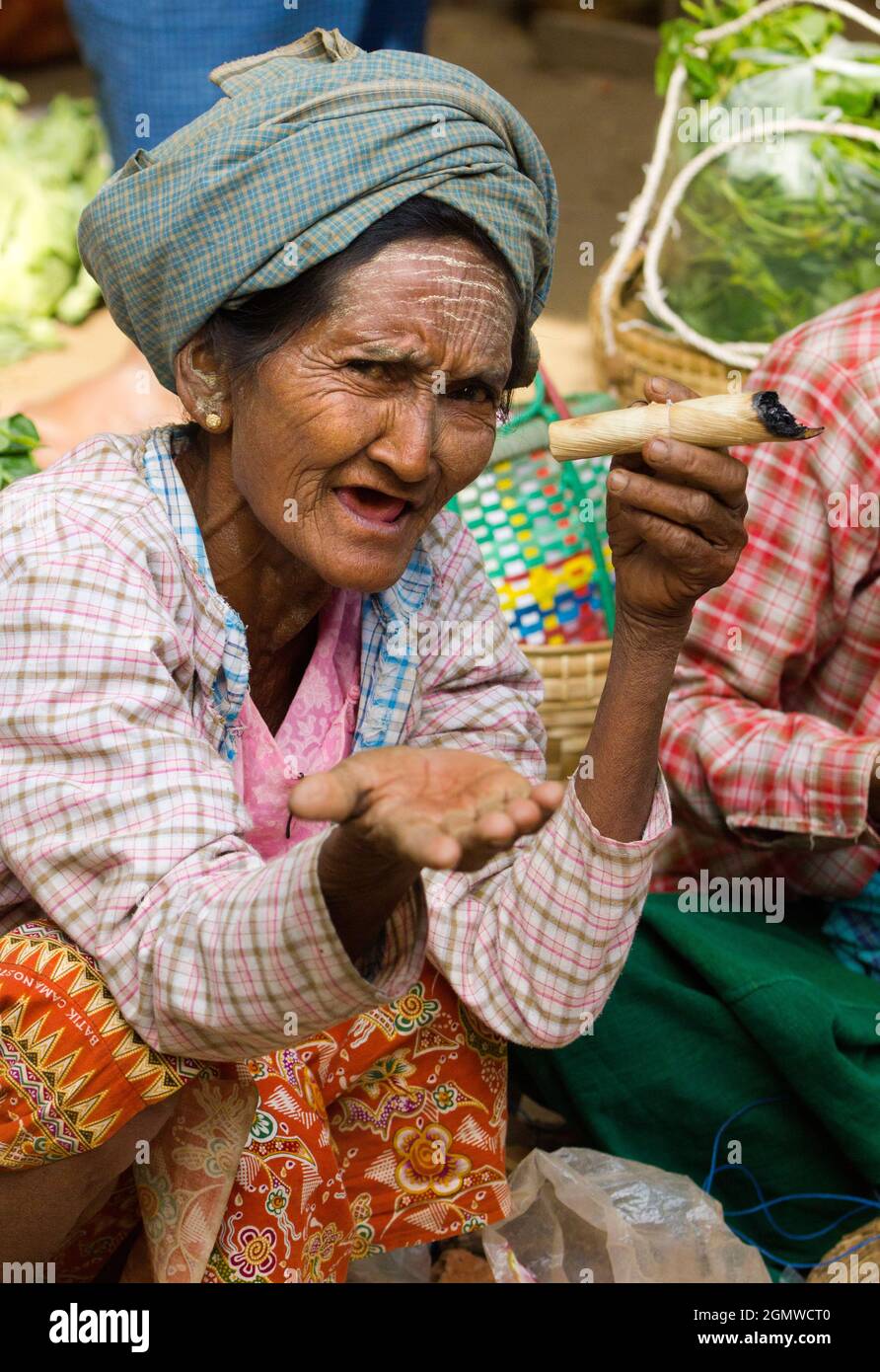 Alte Stammesfrau, mit Thanaka-Make-up, raucht eine unverschämte, selbst angebaute und handgerollte Zigarre in Nyaung - U Market in Mandalay, Myanmar.Verdampfen ist Clea Stockfoto