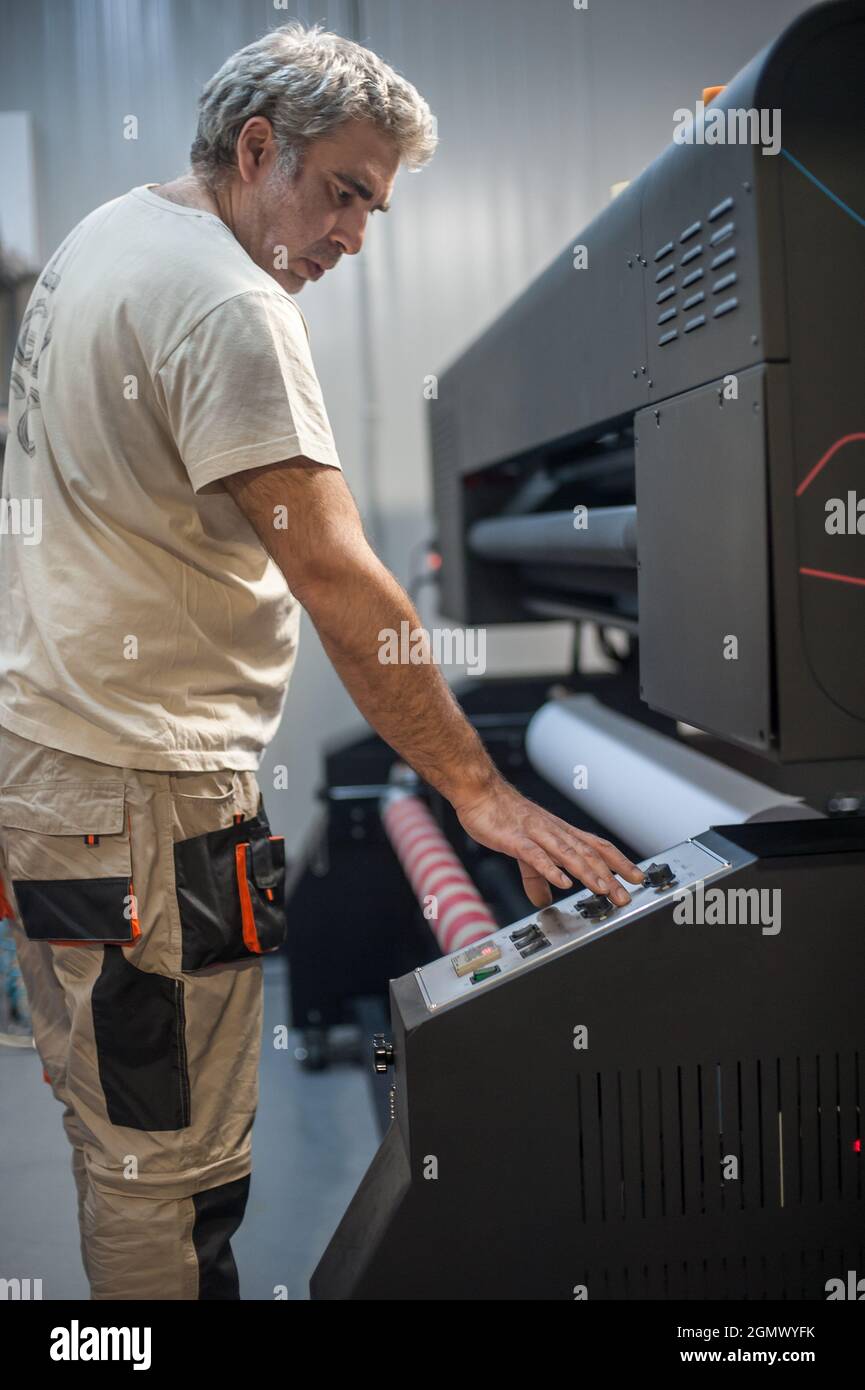 Der Bediener des Technikers wechselt die Papierrolle auf einem großen hochwertigen Industriedrucker und Plottergerät im digitalen Druckereibüro Stockfoto