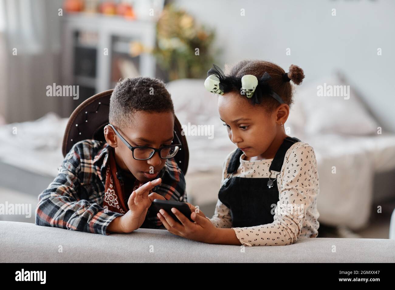Vorderansicht Porträt von zwei afroamerikanischen Kindern, die das Smartphone zusammen in einem gemütlichen Zuhause benutzen, Kopierraum Stockfoto