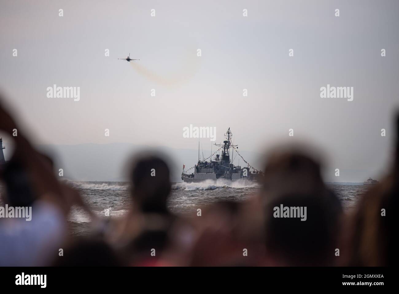 Izmir, Türkei - 9. September 2021: Überfüllte Menschen beobachten Ein Düsenflugzeug und ein Kriegsschiff während Demonstrationen über dem Meer am Tag der Freiheit izmir. Stockfoto