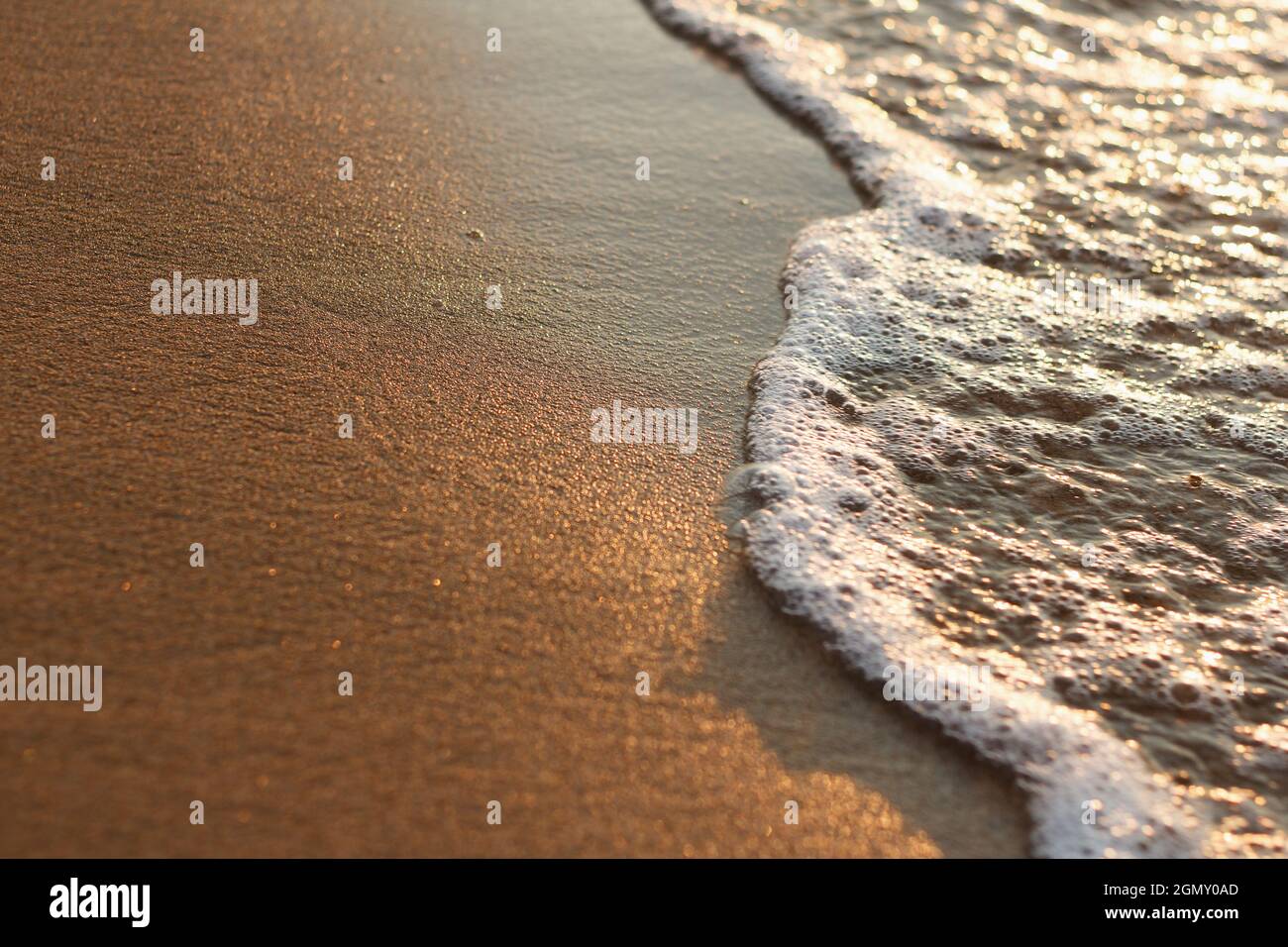 Schäumende Meereswelle und Sand an einem sonnigen Strand Stockfoto