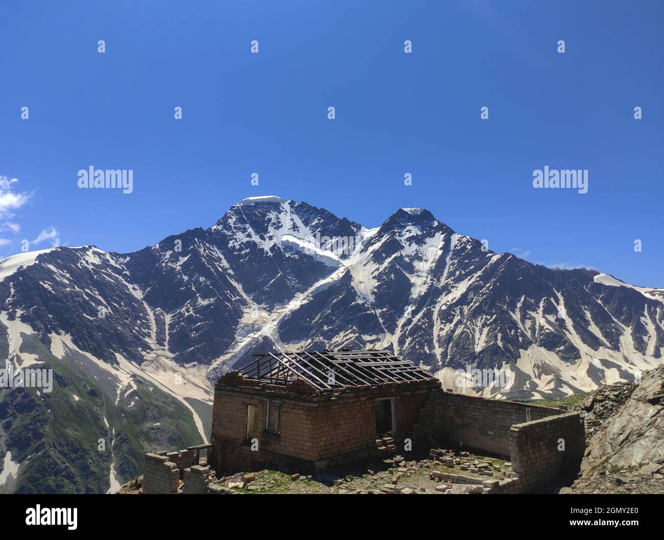 Altes verlassenes Haus in den Bergen. Ruinen einer Hütte ohne Dach auf dem Hintergrund der schneebedeckten Gipfel der Berge. Stockfoto