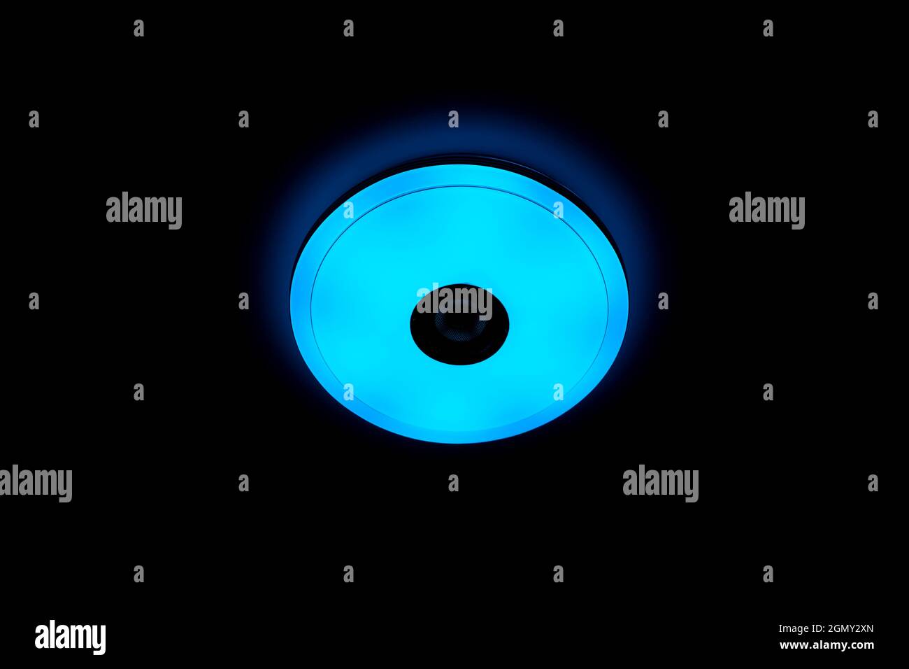 Blaue LED-Deckenleuchte mit integrierten kabellosen Lautsprechern auf schwarzem Hintergrund. Stockfoto