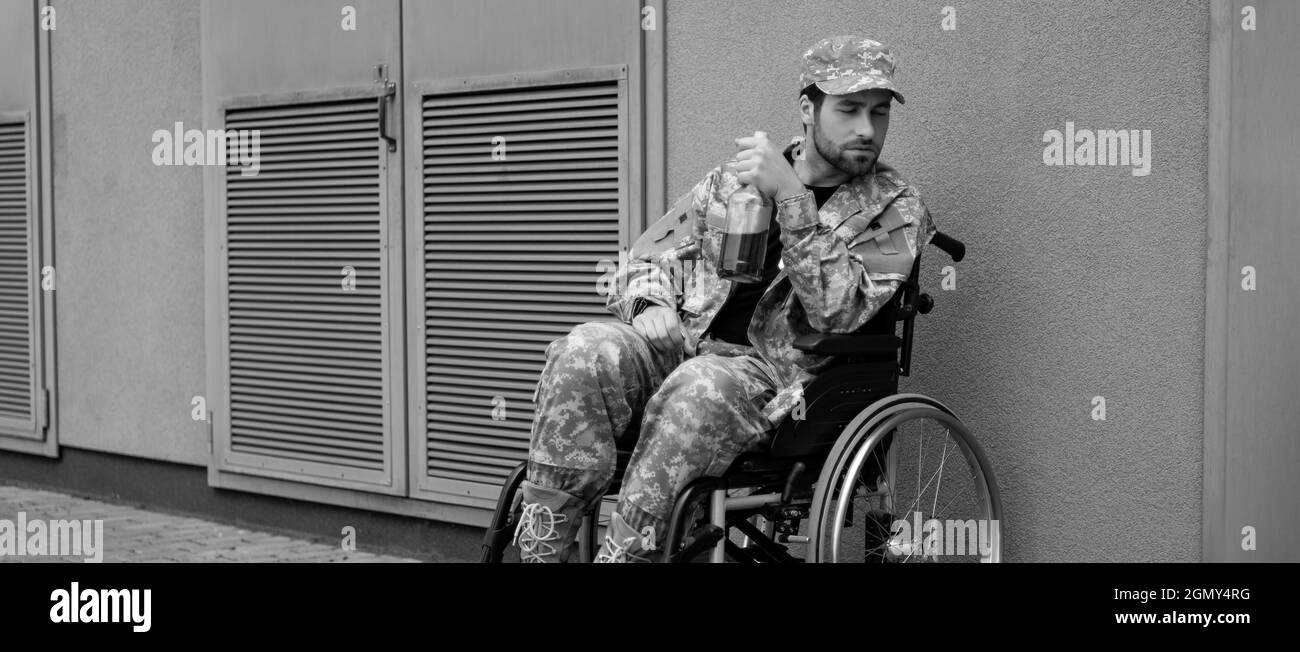 Junger behinderter Soldat, der im Rollstuhl sitzt, mit einer Flasche Alkohol im Freien, Banner Stockfoto