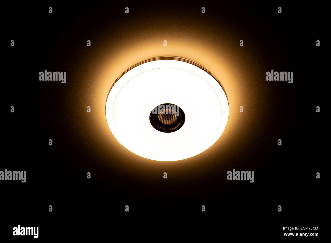 LED-Deckenleuchte mit warmem Licht und integrierten kabellosen Lautsprechern auf schwarzem Hintergrund. Stockfoto
