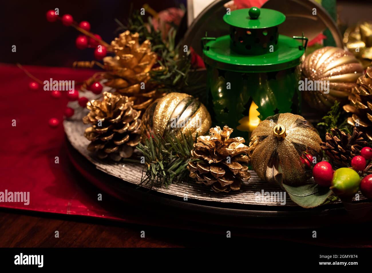 Nahaufnahme eines schwach beleuchteten Weihnachtsdisplays im Mittelpunkt, bestehend aus goldenen Glühbirnen, Kiefernzacken und einer Laterne. Stockfoto