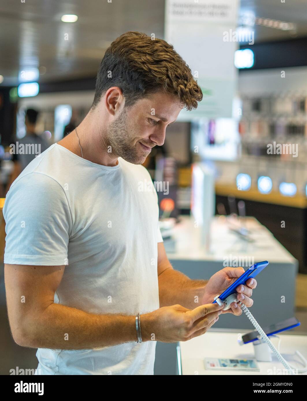 Seitenansicht des Inhalts junger bärtiger männlicher Käufer mit Mobiltelefon und lächelnd zufrieden mit der Qualität, während die Wahl neuer Gadget in modernen Elektronik-Shop Stockfoto