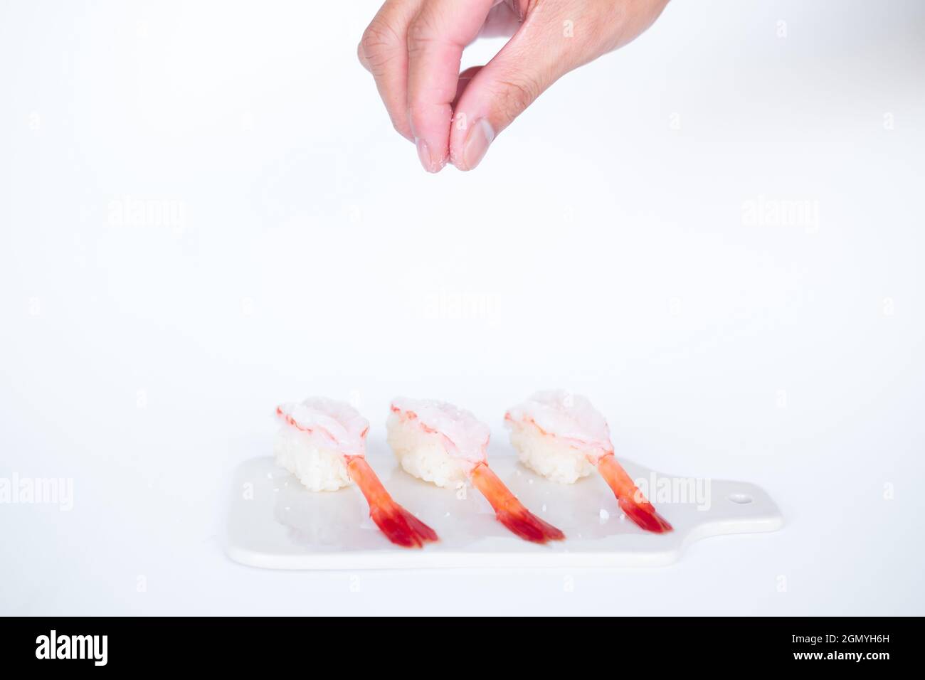 Rohes Shrimp-Garnelen-Sushi im japanischen Restaurant. Sushi - ama Ebi Nigiri auf weißem Brett auf weißem Hintergrund. Der Koch gießt Salz. Hochwertige Fotos Stockfoto