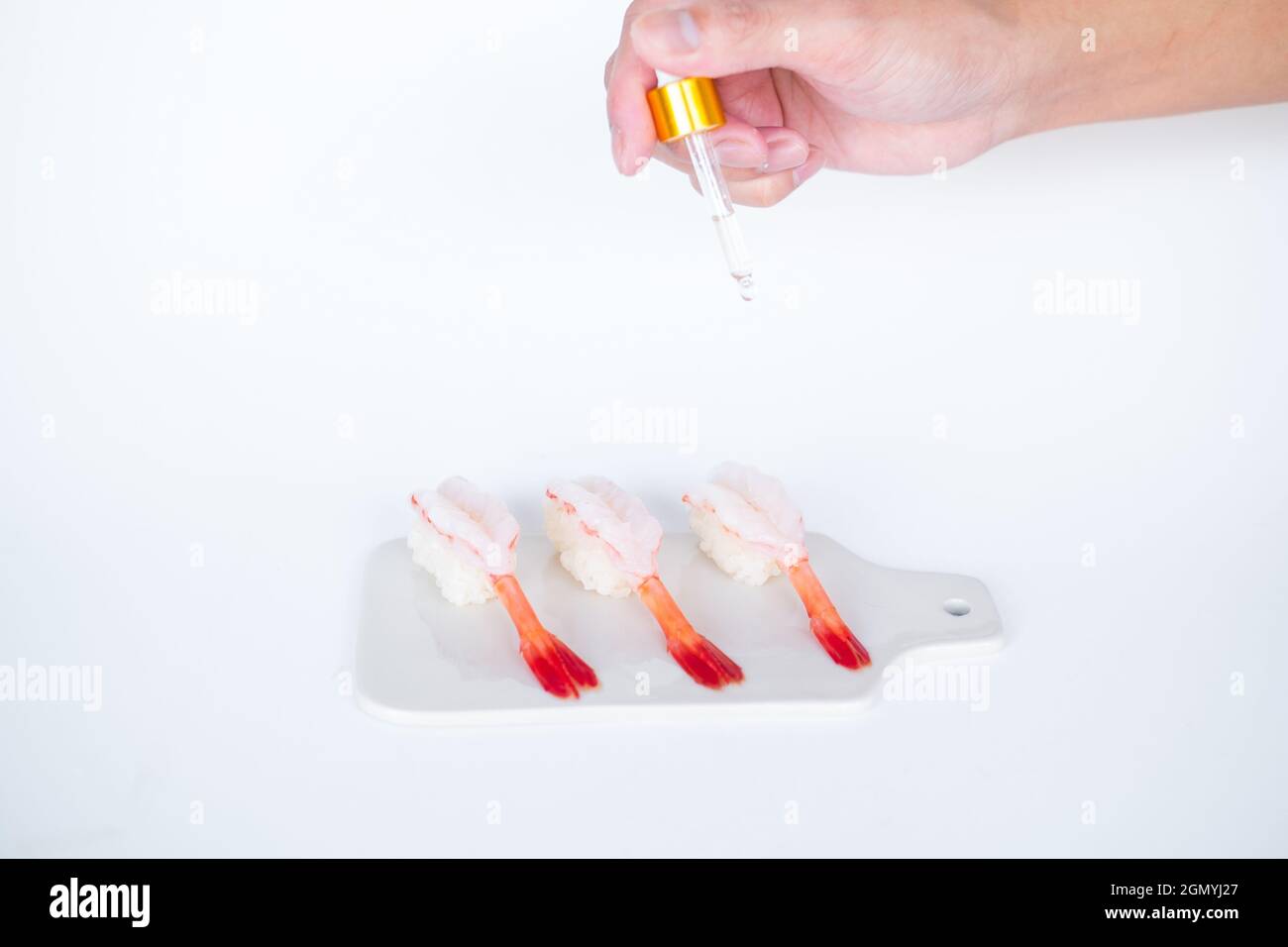 Rohes Shrimp-Garnelen-Sushi im japanischen Restaurant. Sushi - ama Ebi Nigiri auf weißem Brett auf weißem Hintergrund. Cook tropft die Sauce. Hochwertige Fotos Stockfoto