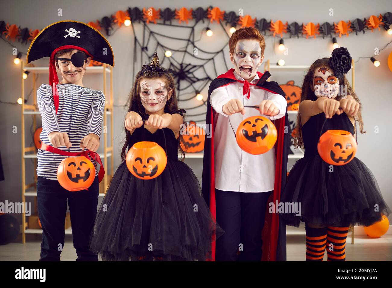 Vier Kinder in Karnevalskostümen und mit gruseliger Schminke reichen ihre Eimer-Kürbisse zur Kamera. Stockfoto