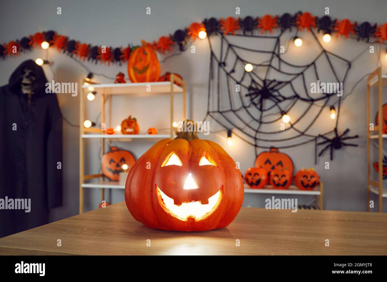 Nahaufnahme von leuchtendem Halloween-Kürbis, der auf dem Tisch im Zimmer mit anderen Urlaubsdekor steht. Stockfoto