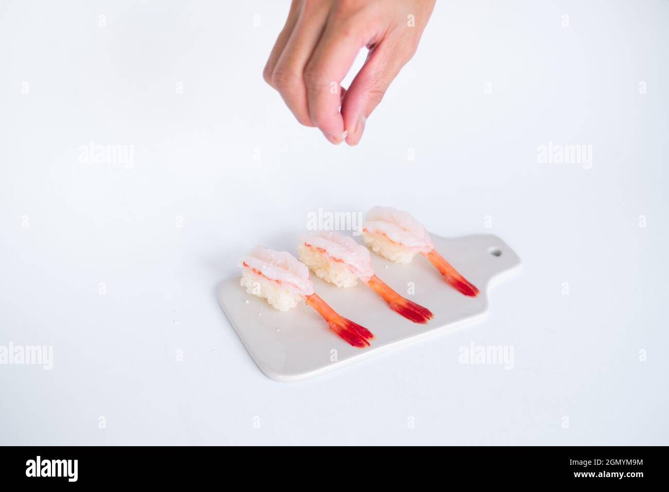 Rohes Shrimp-Garnelen-Sushi im japanischen Restaurant. Sushi - ama Ebi Nigiri auf weißem Brett auf weißem Hintergrund. Der Koch gießt Salz. Hochwertige Fotos Stockfoto
