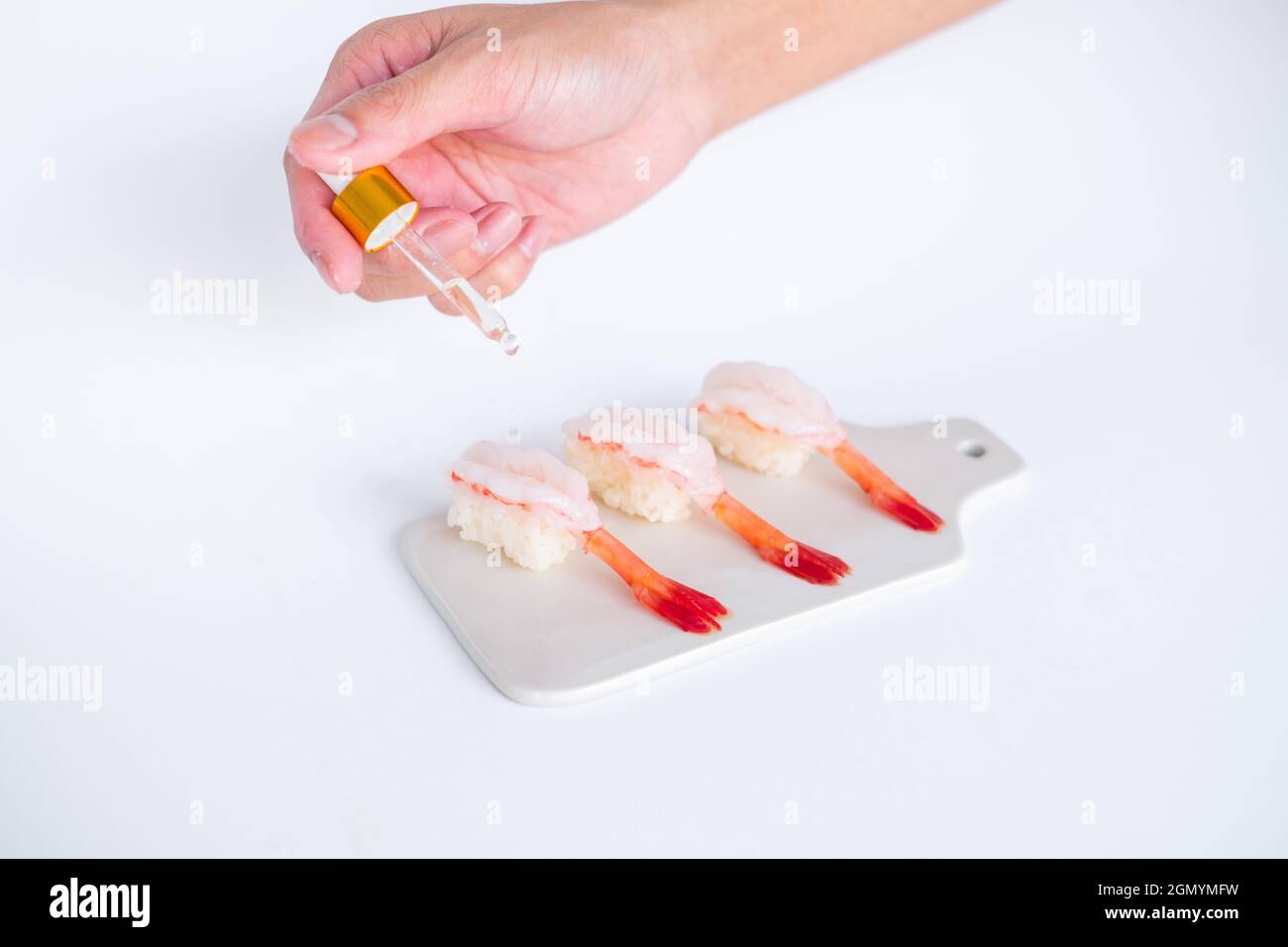 Rohes Shrimp-Garnelen-Sushi im japanischen Restaurant. Sushi - ama Ebi Nigiri auf weißem Brett auf weißem Hintergrund. Cook tropft die Sauce. Hochwertige Fotos Stockfoto