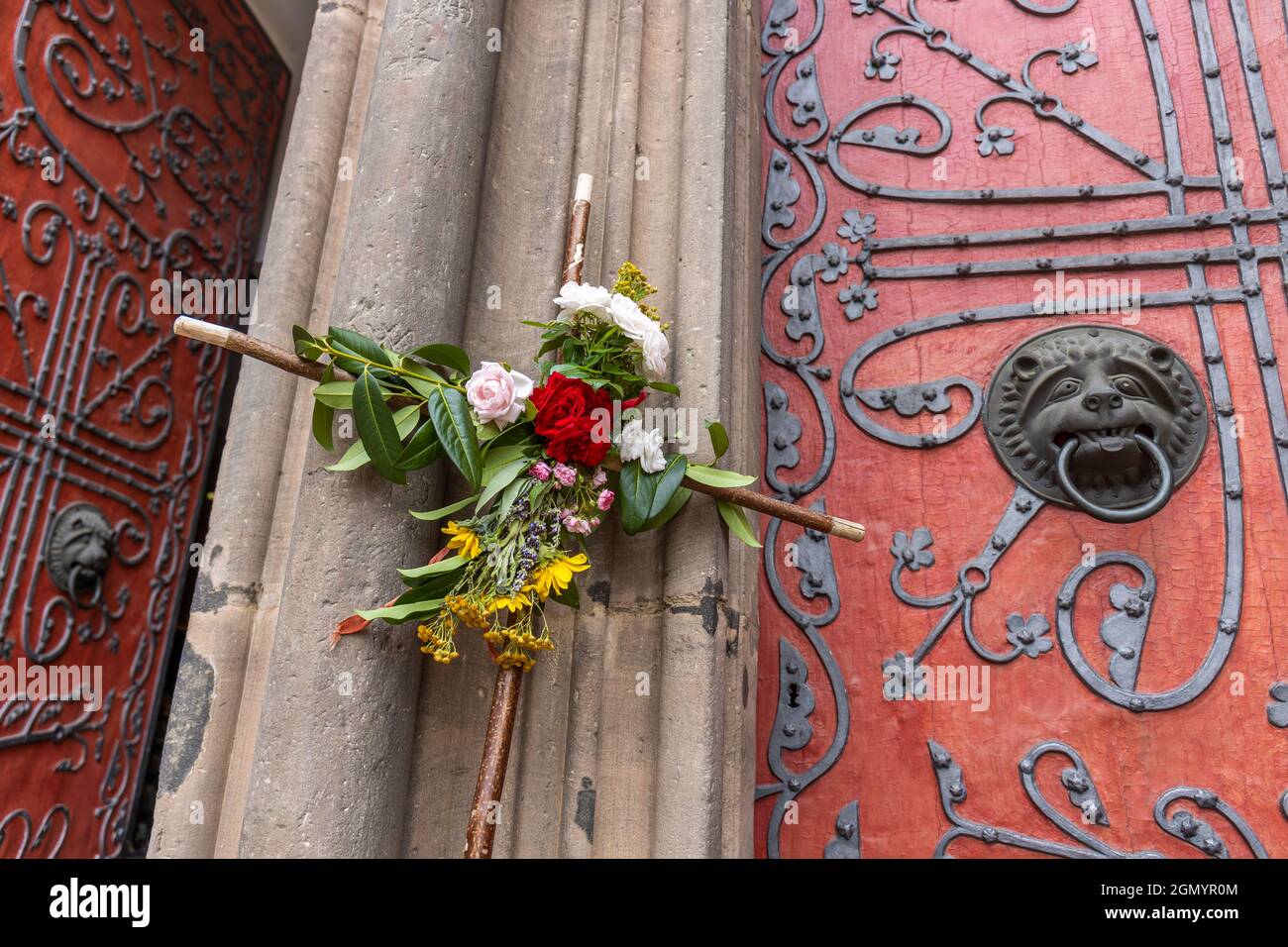 Das mit Blumen geschmückte hölzerne Pilgerkreuz lehnt sich an das Hauptportal der St. Elisabethkirche in Marburg, Deutschland, einem wichtigen Pilgerziel Stockfoto