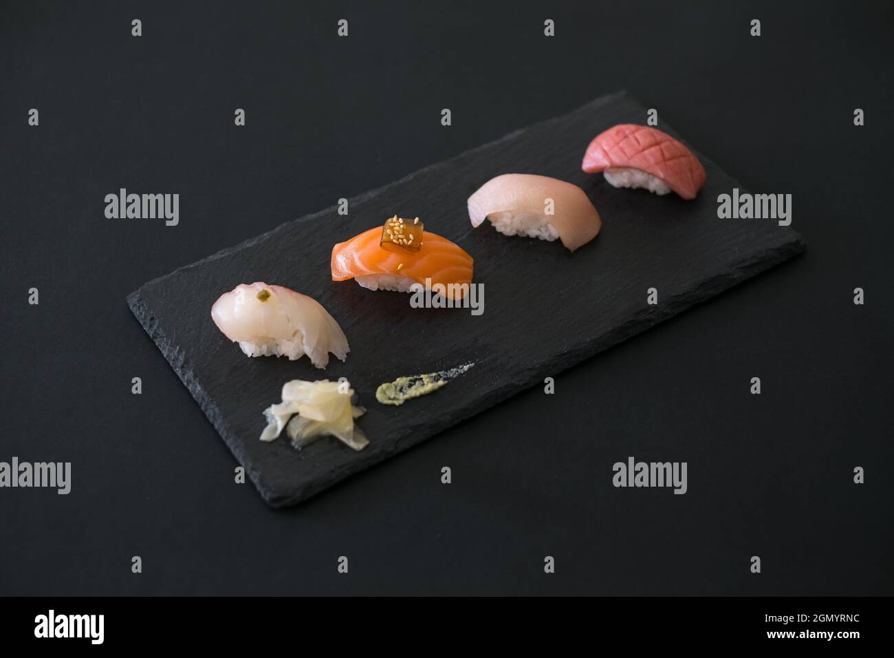 Sushi-Set auf schwarzem Tablett. Vier verschiedene Sushi-Stücke auf schwarzem Schiefer mit Ingwer. Traditionelles japanisches Essen auf schwarzem Hintergrund. Stockfoto