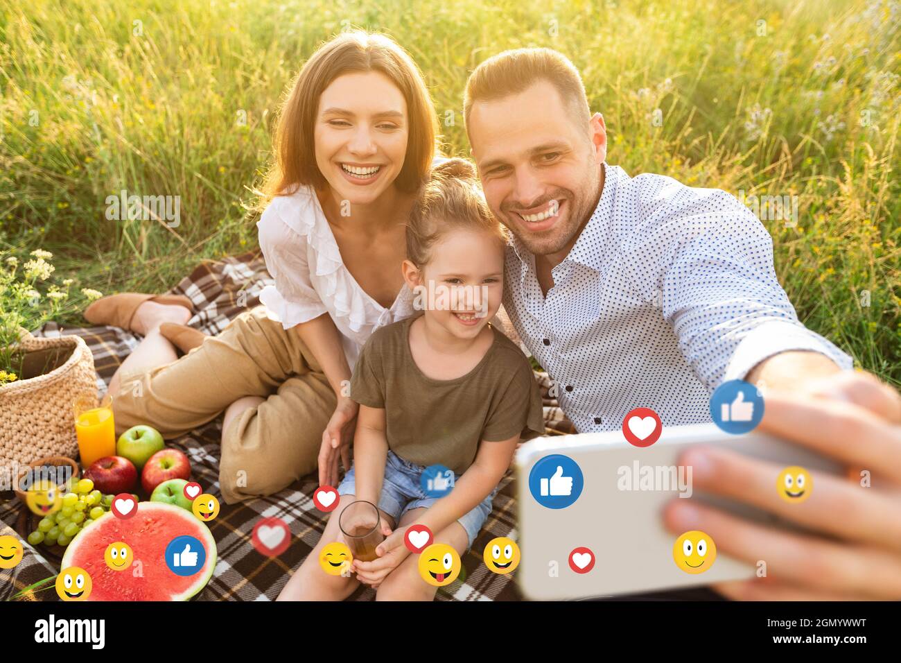 Fröhliche junge europäische Familie mit kleiner Tochter auf Picknick und Selfie für soziale Netzwerke im Freien Stockfoto